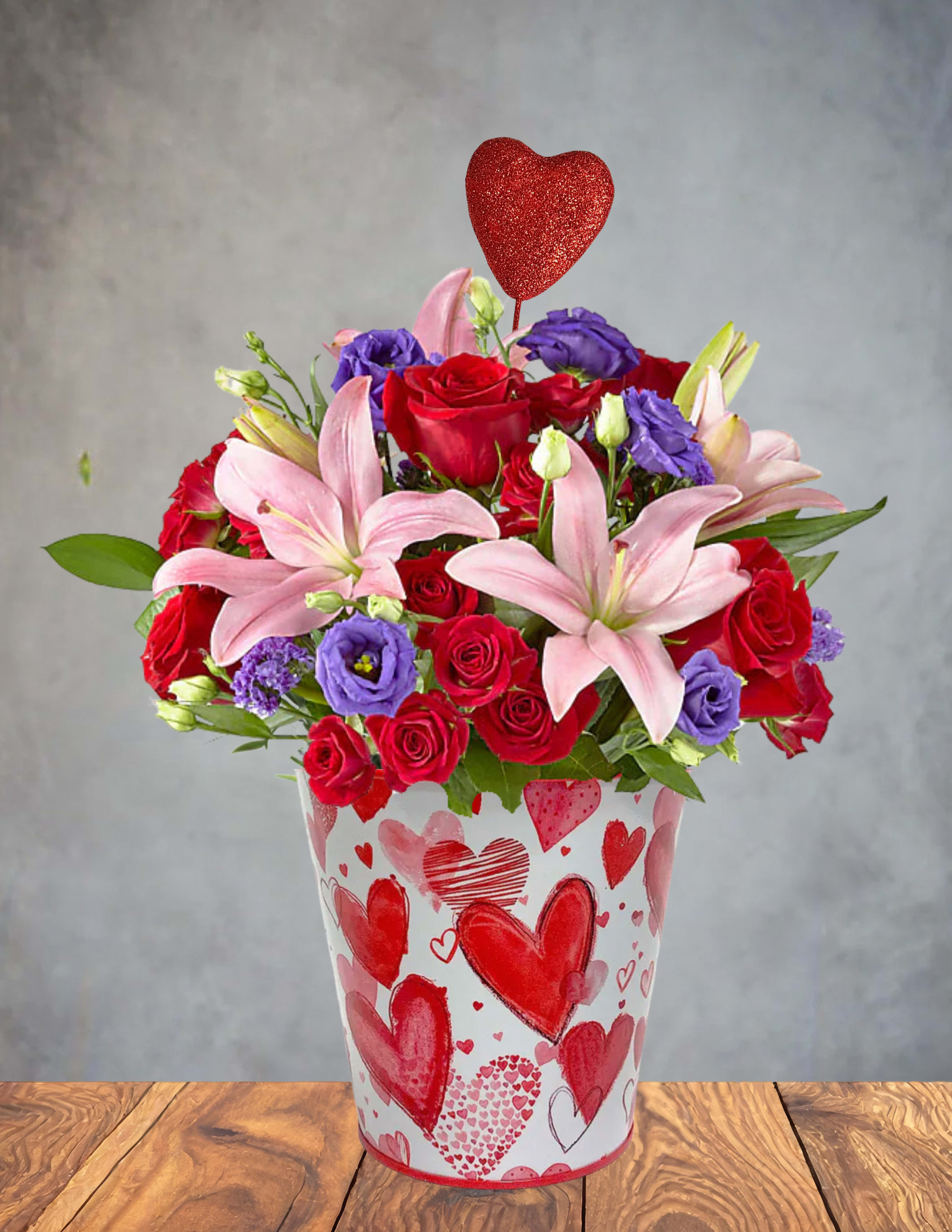  Romance Rewind   -  Romance Rewind   Step back into the sweetest moments of love with this lush, memory‑soaked bouquet. Featuring blushing pink lilies, passionate red roses, and dreamy purple lisianthus, each bloom whispers of first kisses, handwritten notes, and heart‑fluttering glances.  Nestled in a whimsical heart‑patterned vase and crowned with a glittering red heart, this arrangement is perfect for rekindling old flames or celebrating timeless devotion. Whether it’s Valentine’s Day or just because, Romance Rewind brings the past into the present—beautifully.