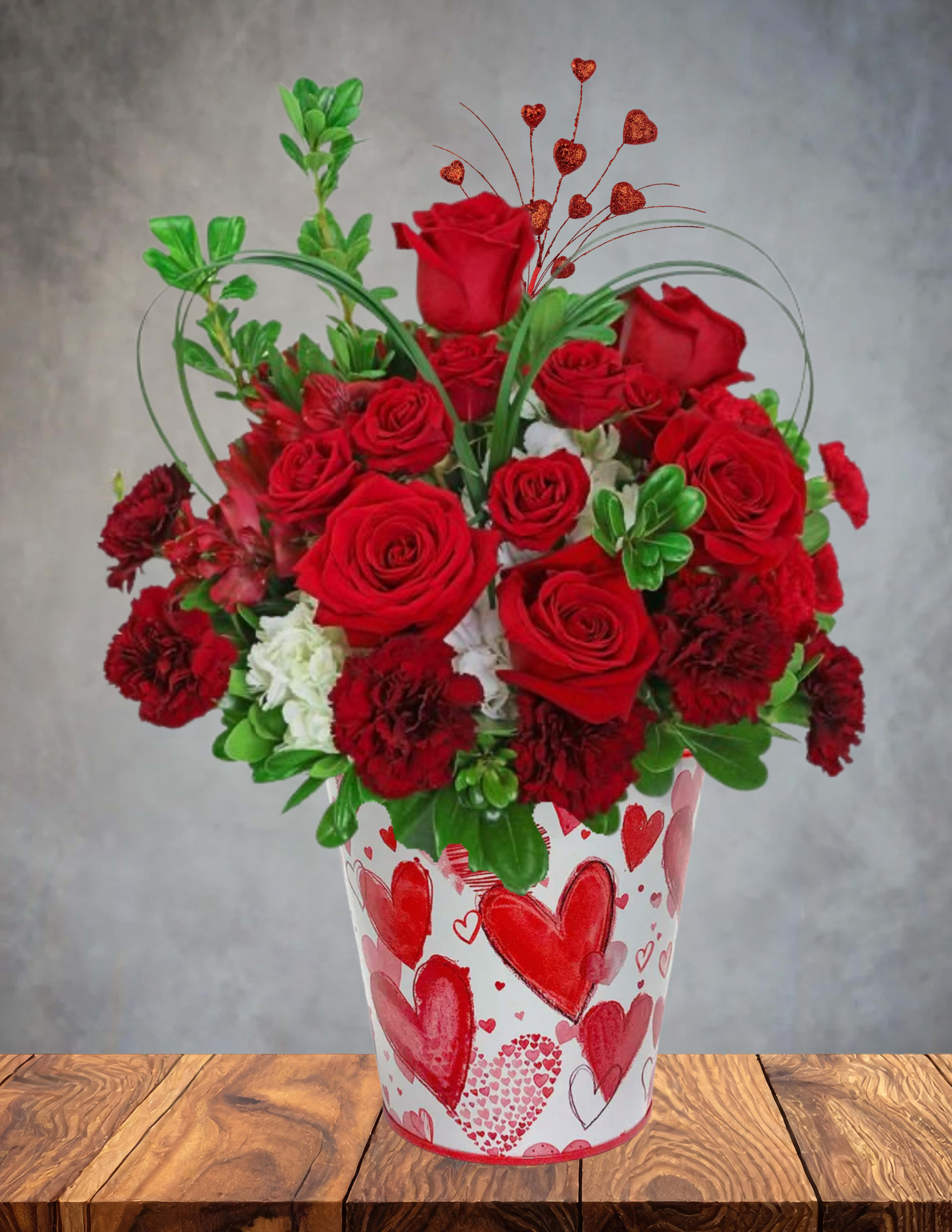 Queen of Hearts   - ️ Queen of Hearts   Bold, elegant, and irresistibly charming, Queen of Hearts is a floral tribute fit for royalty. This enchanting design overflows with lush roses and ruffled carnations, creating a rich tapestry of color and texture. A full, luxurious hydrangea adds softness and volume, while handcrafted hearts made from lily grass give the arrangement its signature whimsical touch.  Presented in a sweet heart‑patterned bucket, this piece blends romance with playful artistry—perfect for Valentine’s Day, anniversaries, or anyone who deserves to feel like the reigning queen of your heart.