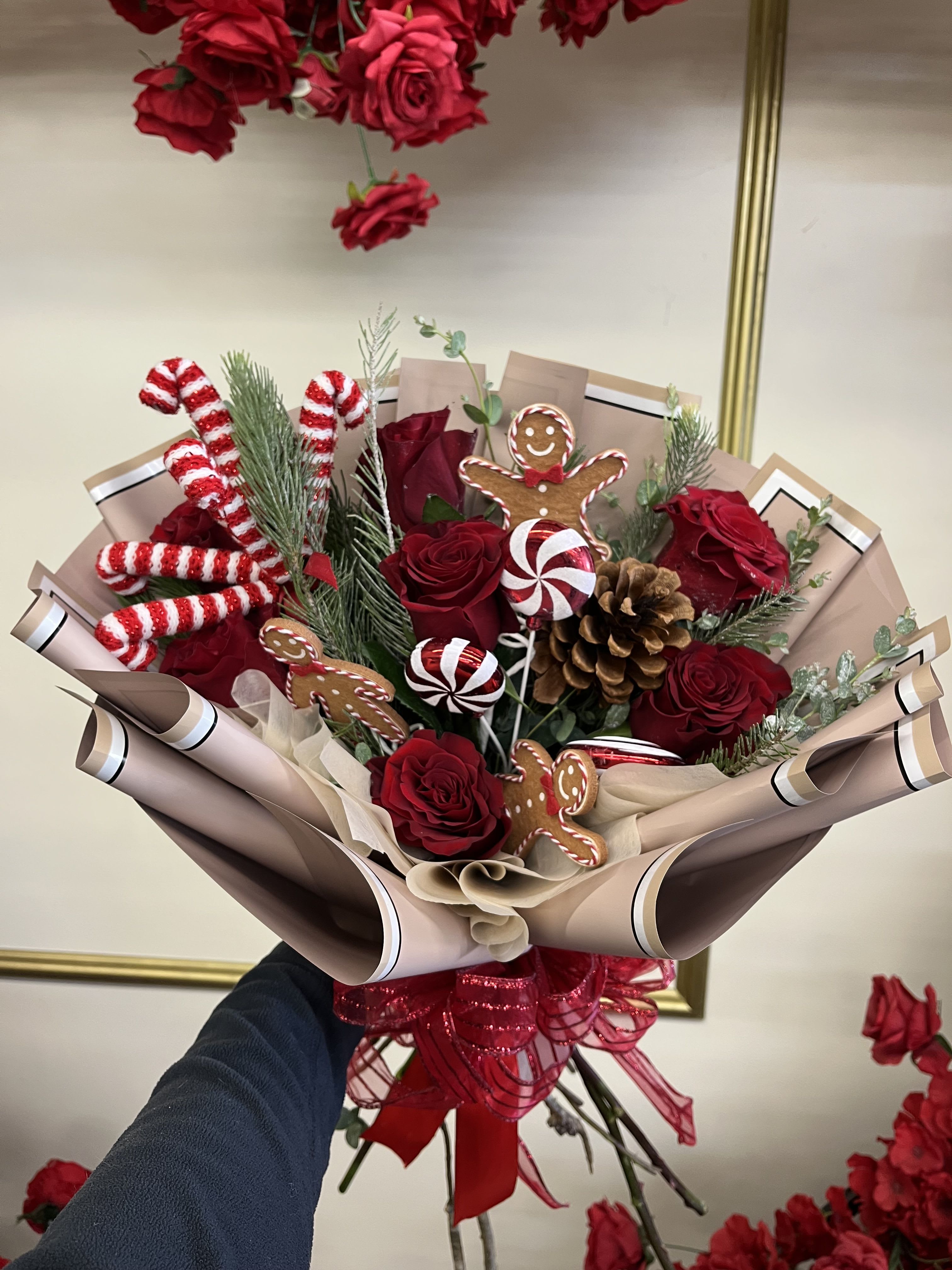 Gingerbread Red Bouquet  - Our Gingerbread Cheer Bouquet brings the magic of Christmas to life! Featuring rich red roses, festive pine, candy-stripe accents, pinecones, and adorable gingerbread details, the perfect holiday treat to gift or enjoy at home