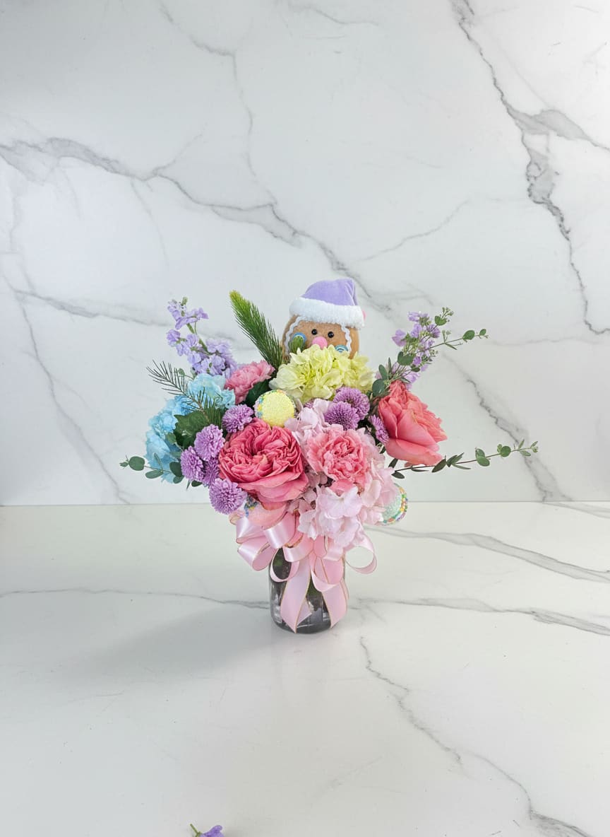 Candy Wonderland Christmas Vase - A pastel holiday mix featuring soft roses, carnations, hydrangeas and playful accents tucked around a sweet gingerbread character. Light, colorful, and whimsical.