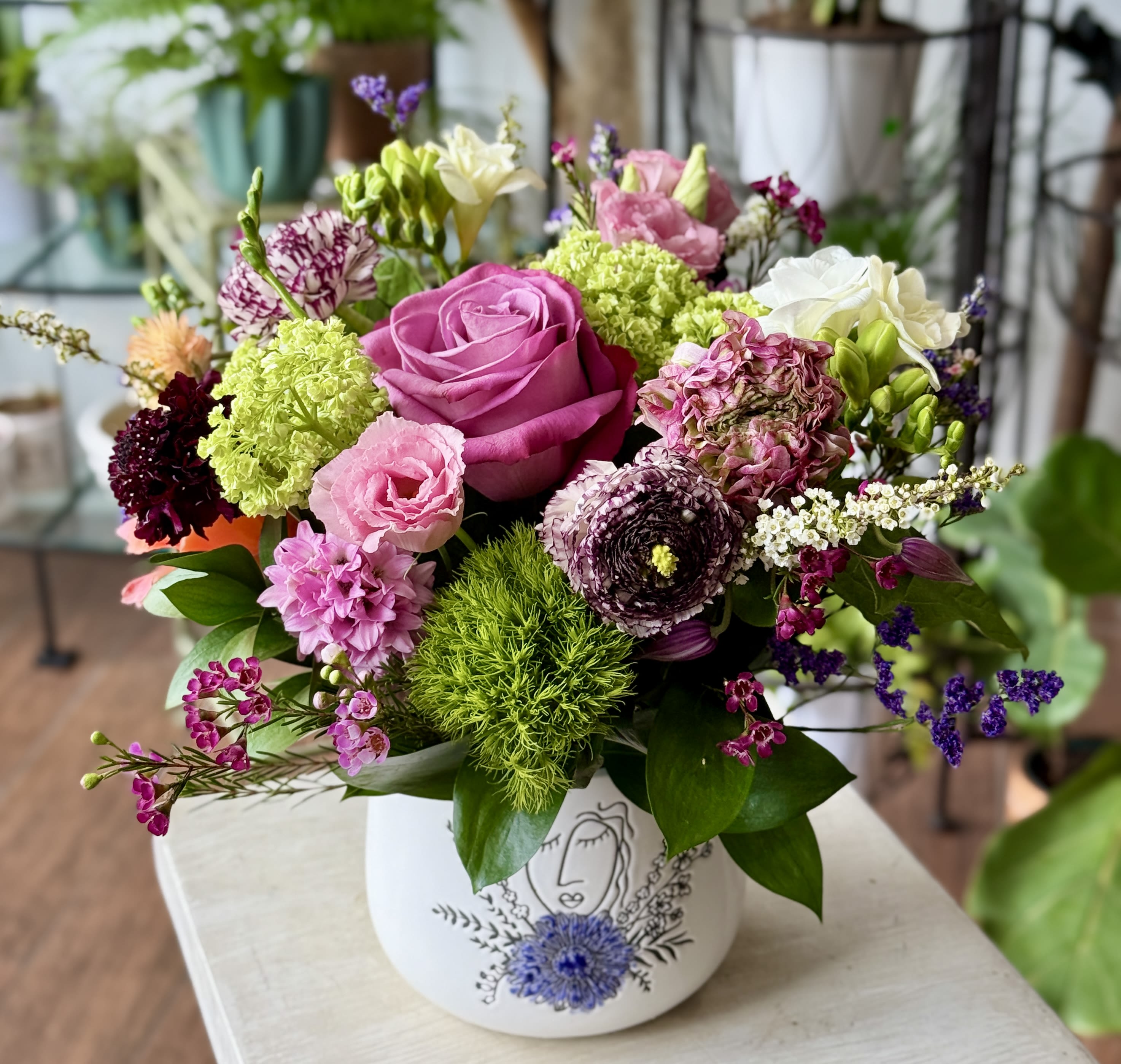 Violet - Interesting and colorful selection of seasonal blooms in a ceramic vase. 
