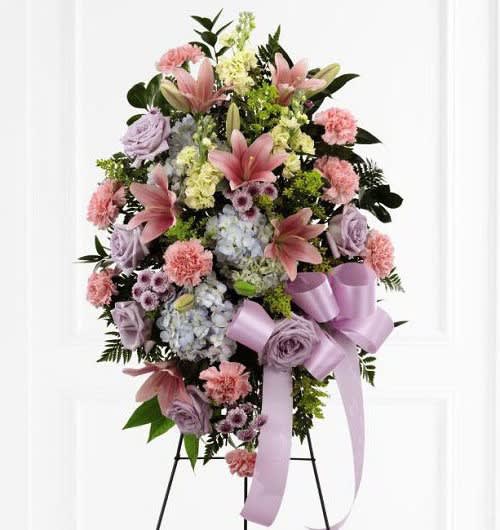 Lovely Blessings - Easel spray designed with pink lillies, carnations, hydrangea and pretty lavender/pink filler flowers with a nice variety of greens and a large flowing lavender/light pink bow added 