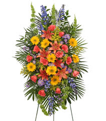 VIBRANT FLORAL EXPRESSION Standing Funeral Spray - A beautiful bright mixture of gerbera daisies, lilies, delphinium, spray roses, mini carnations, filler flowers and a pretty variety of fresh greens. This one is quite the display for your loved one in honor of their sweet memory and soul.
