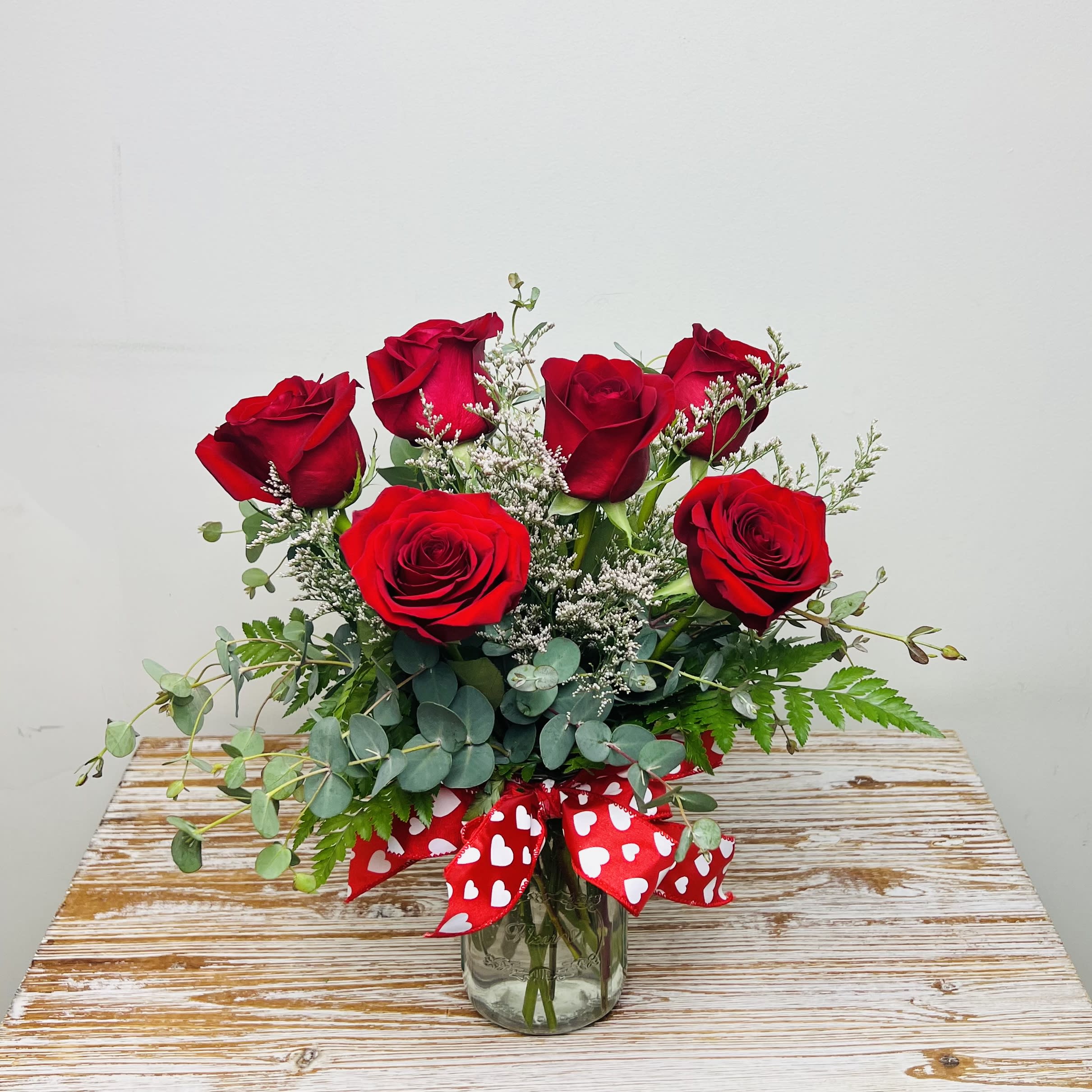 Cupid’s Arrow - Cupid’s Arrow has struck the heart of your Valentine! Cupid’s Arrow consists of 6 beautifully arranged red roses accented with greens and limonium in a mason jar vase with a Valentine’s heart ribbon.   Approximately 14” Tall 