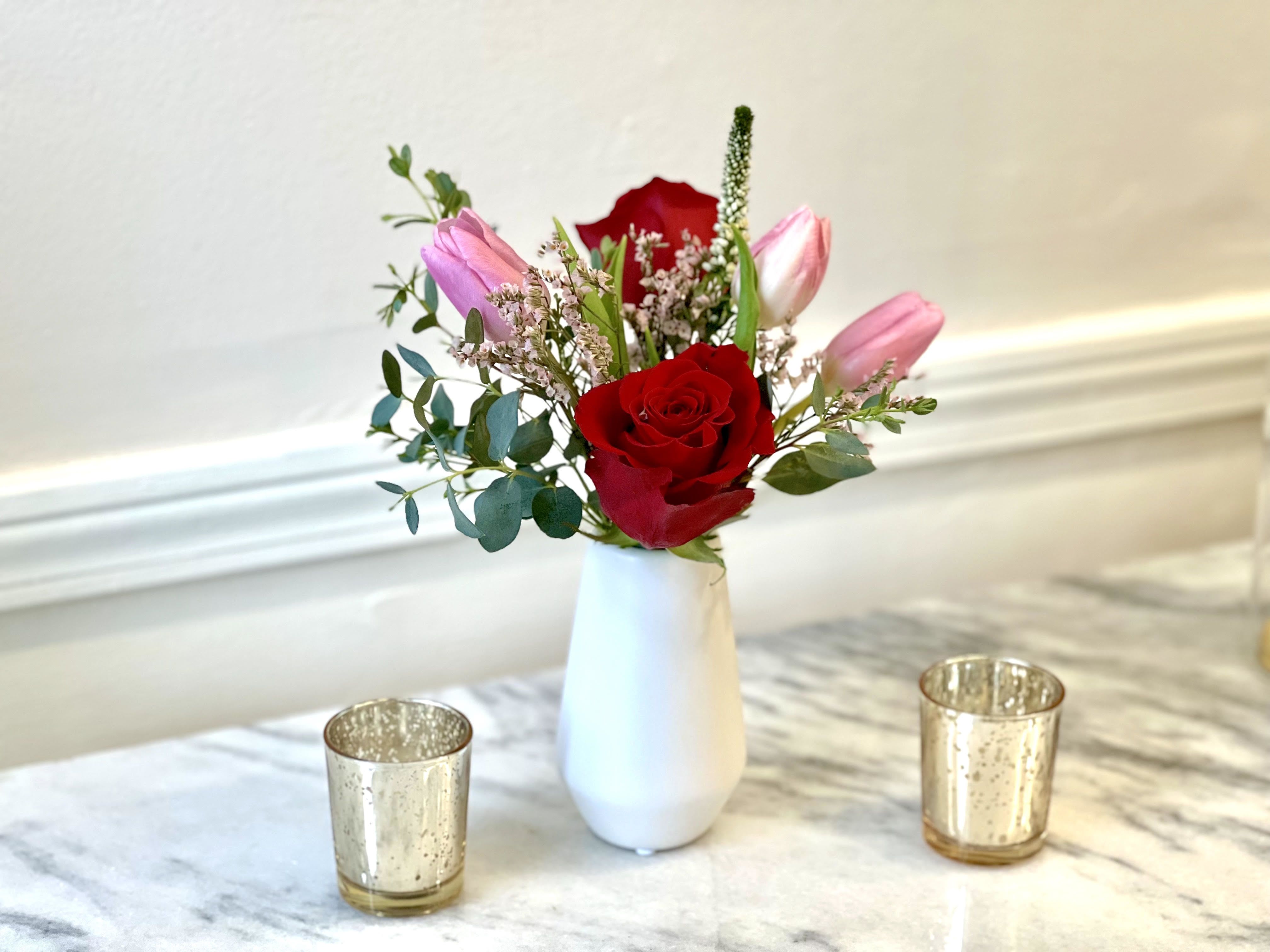 Sweet Bliss - Mini Size - It may be small but it's full of LOVE! Our Sweet Bliss mini is perfect for a daughter, Galentine or new love. A sleek white bud vase filled with deep red roses, bright pink tulips, Eucalyptus and accent blooms.  Only available now through February 14. Arrangement is approximately 9" tall and 3" wide. 