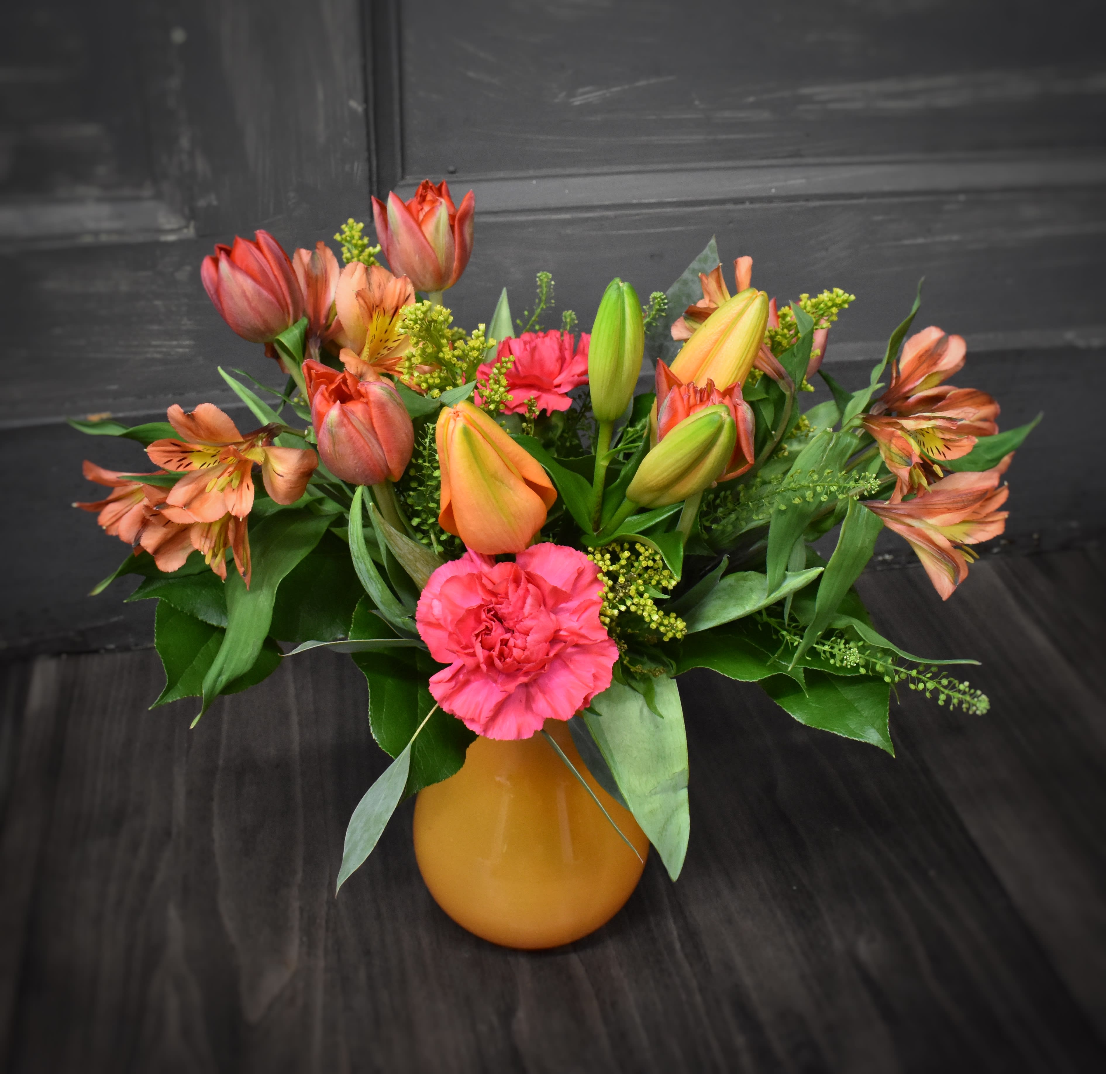 Pantown Party - A lovely orange vase filled with a variety of flowers in a cheerful and bright color scheme. 