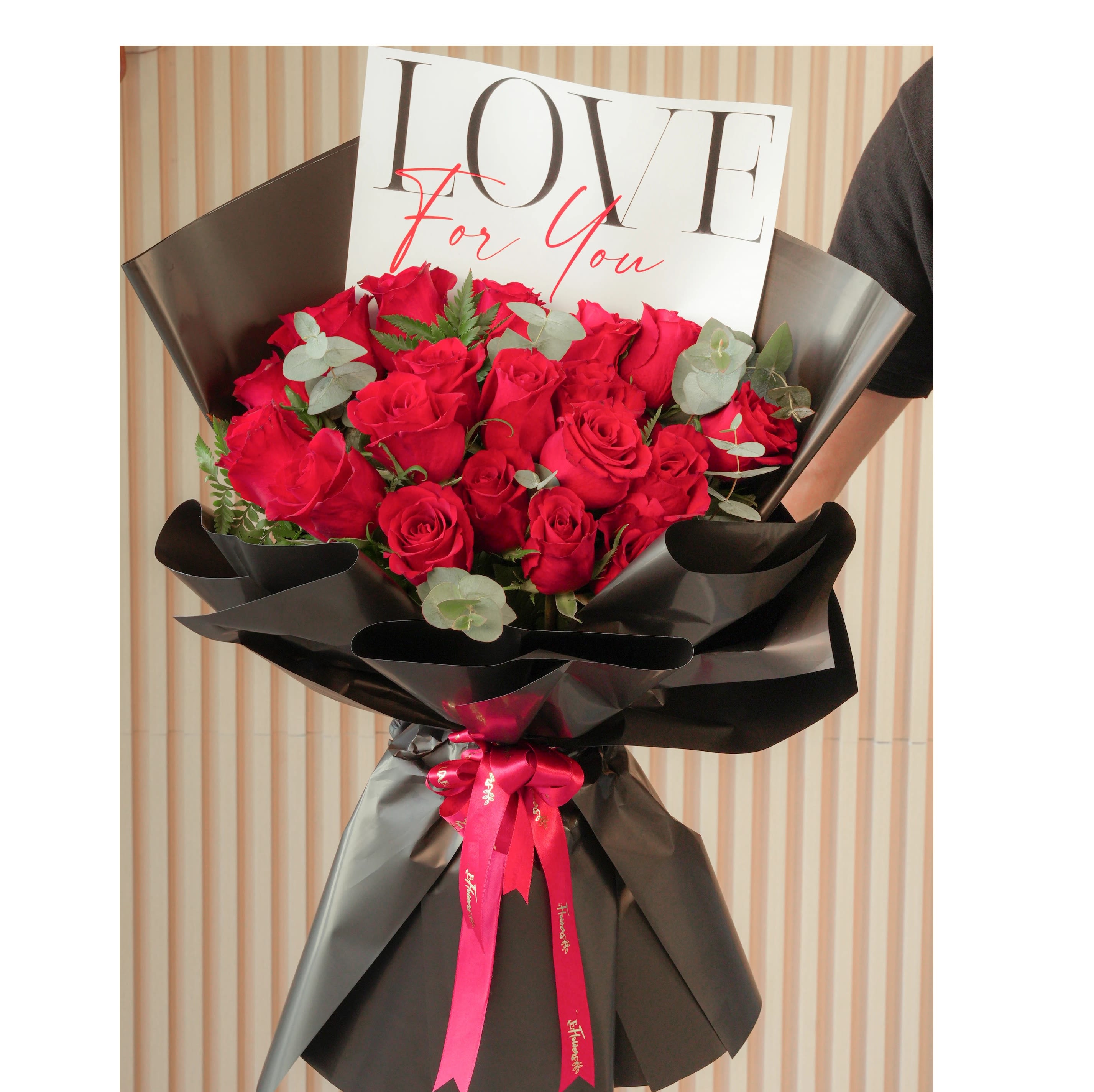       24 Red Roses ( Love For You ) Wrapped  Bouquet  - This elegant bouquet of 24 red roses, accented with lush green fillers and wrapped in sophisticated black paper, is a timeless expression of love and admiration. Tied with vibrant red ribbons, this bouquet is perfect for romantic gestures, heartfelt surprises, or special celebrations.Red roses symbolize deep love, passion, and devotion, while the green fillers add a fresh and natural charm. The black wrapping adds a modern and striking contrast, beautifully complemented by the bold red ribbons. This bouquet is a perfect way to share your emotions and create unforgettable moments with someone special. Standard: 24 Roses. Deluxe:36 Roses. Premium: 48 Roses(.Choose roses colour ) 
