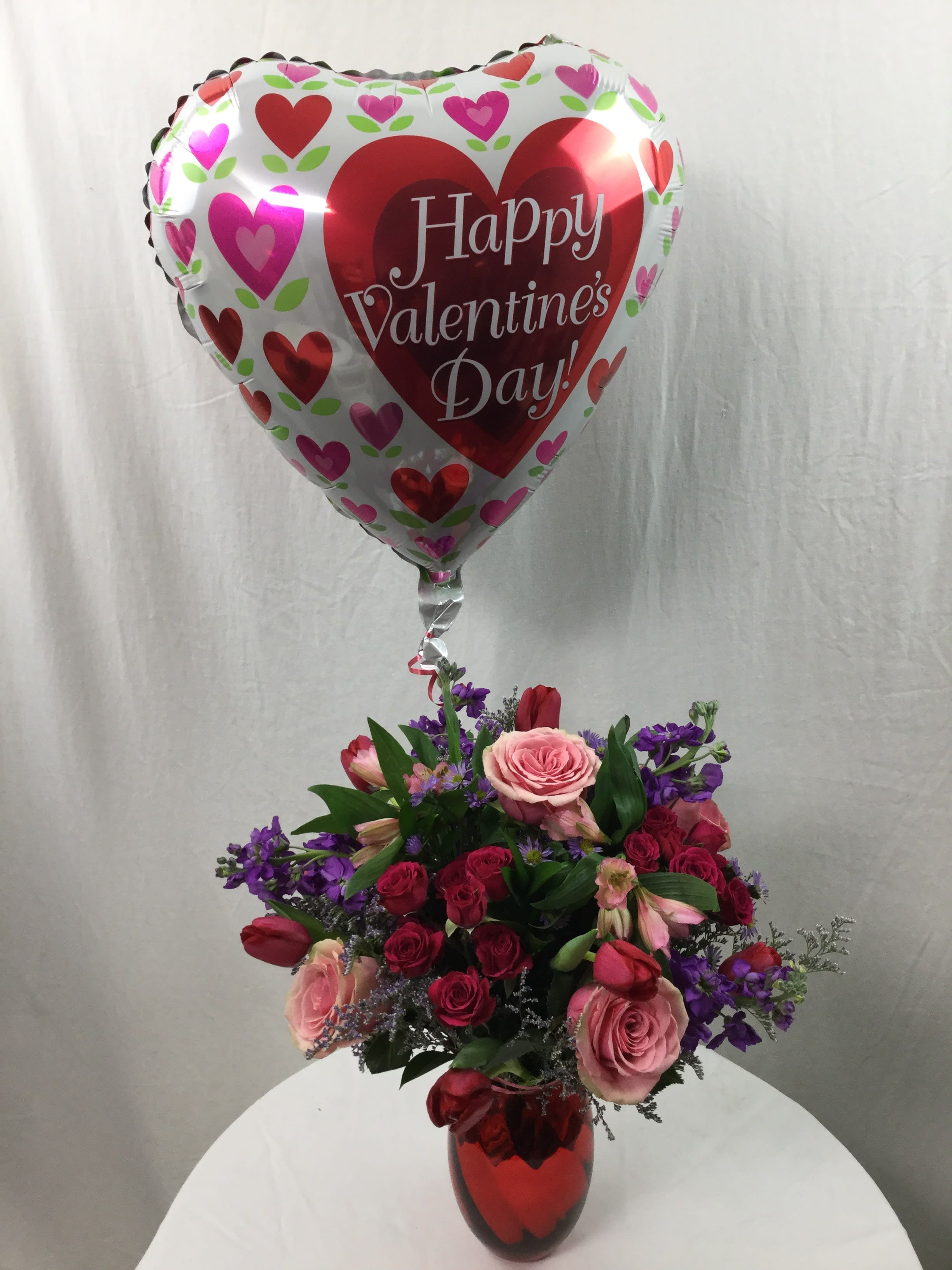 Lovable Bouquet with Mylar - This beautiful bouquet is hand-crafted and designed with love in mind. The vase is a keepsake that she can reuse all year long. The blooms are fresh, bold and gorgeous. The mylar balloon is a perfect little touch to the already perfect bouquet. Due to possible manufacturing delays due to covid, the red vase may be substituted with a clear glass vase topped off with a red bow.