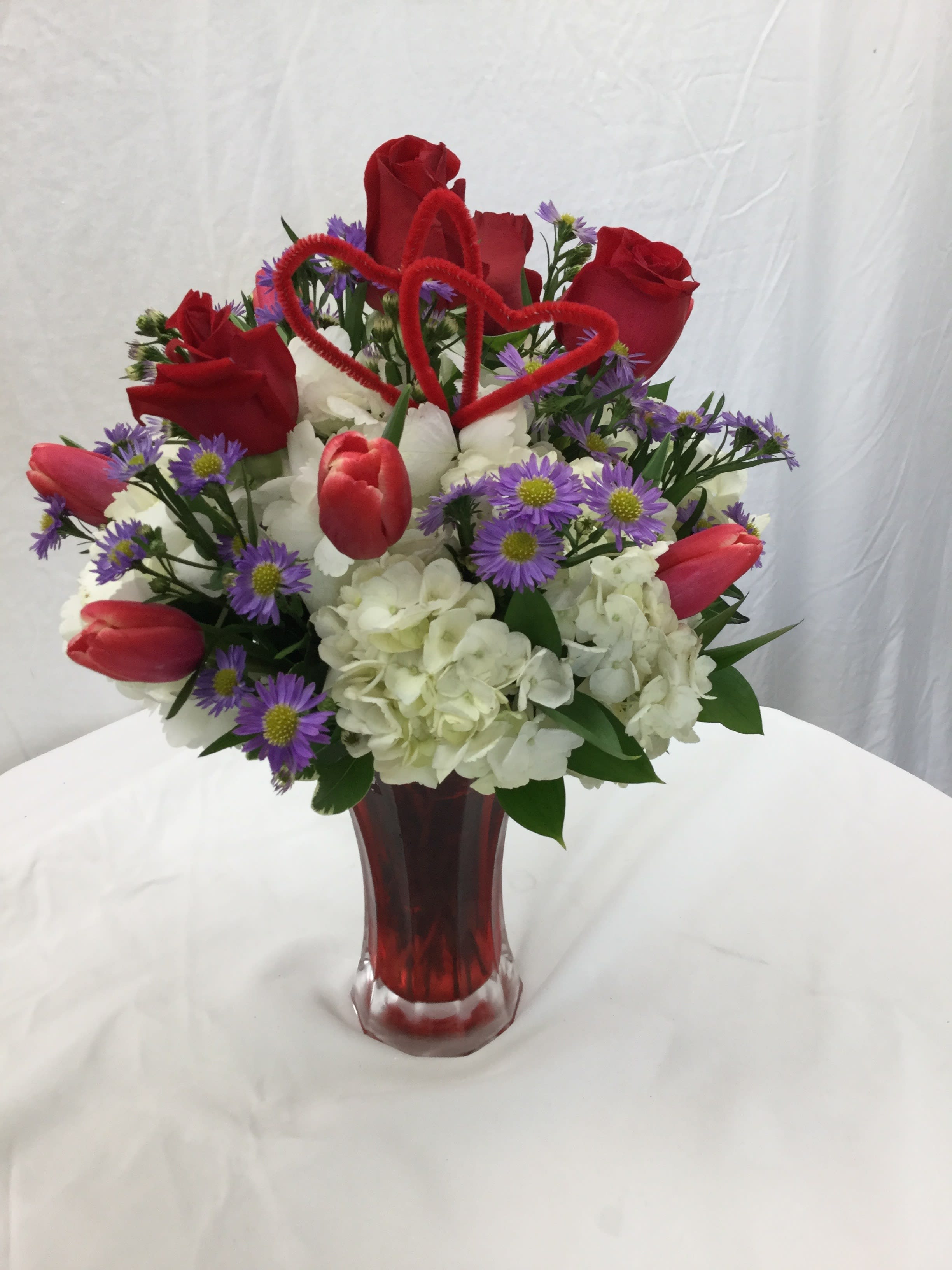 Cupid's Excellence  - Hand-crafted and designed with love in mind, this bouquet will put a smile in your loved ones heart. Includes heart decor and red glass vase.