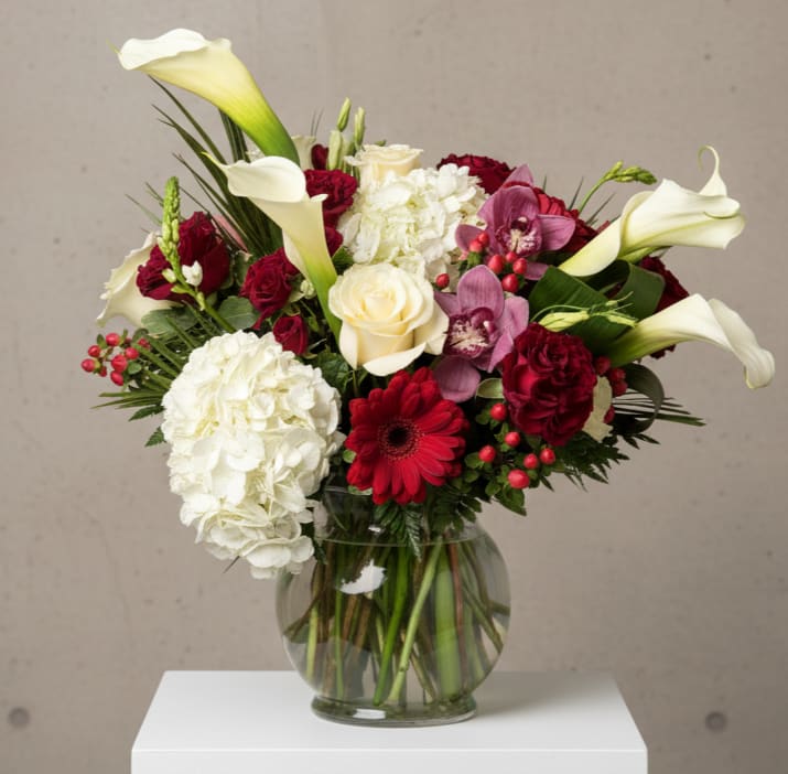 Crimson Embrace - Crimson Embrace is a stunning blend of rich reds, soft ivories, and graceful whites, designed to make a lasting impression. Created here at Pearland Flower Shop it features elegant calla lilies, classic roses, lush hydrangea, vibrant gerbera daisies, and delicate orchids.   This arrangement balances romance with timeless sophistication. Accented with seasonal greenery and berries, it’s perfect for Valentine’s Day, anniversaries, expressions of love, or meaningful moments of sympathy.  Each bouquet is handcrafted with care using the freshest blooms available.