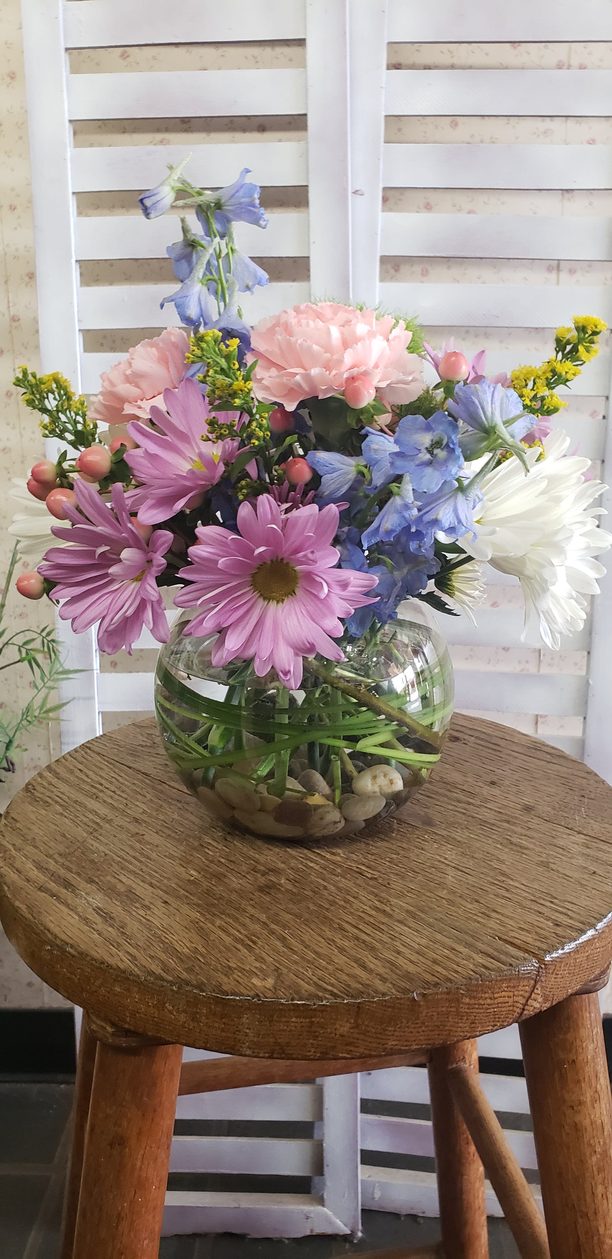 Abundant Life - Bubble bowl with river rocks hold a beautiful assortment of wild flowers such as delphinium, daisies, carnations, hypericum berries and solidago.