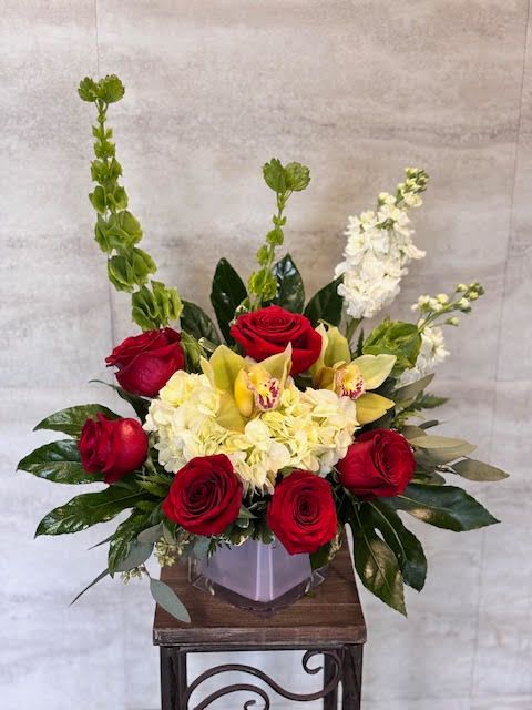 Hugs &amp; Kisses - A compact, elegant floral arrangement featuring deep red roses, soft yellow orchids, creamy hydrangeas, and fresh green accents, artfully arranged in a clear square vase for a classic, romantic look. 