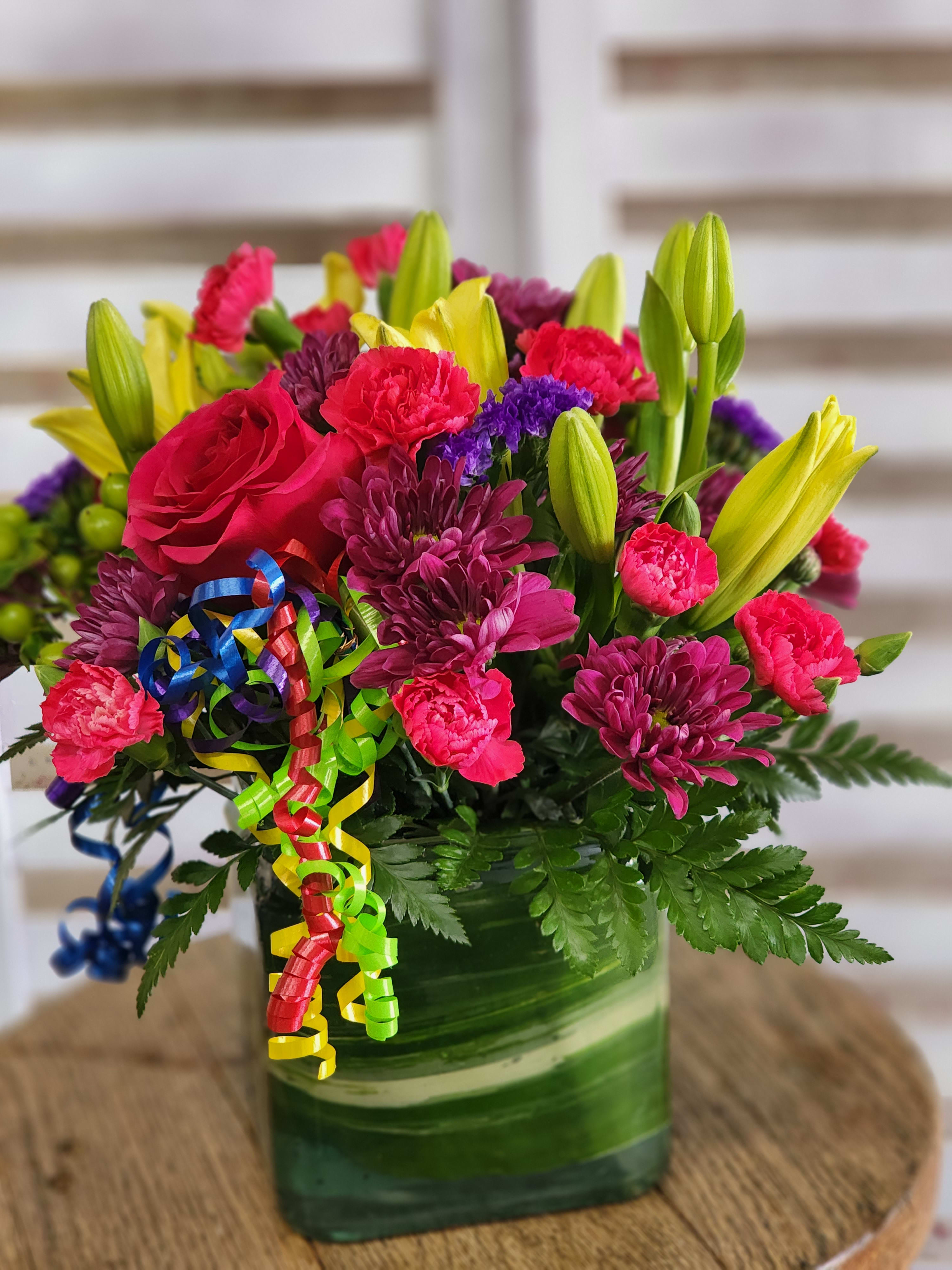 Square Dance - Yellow lilies, paired with hot pink roses and mini carnations along with pops of purple in a leaf lined cube.