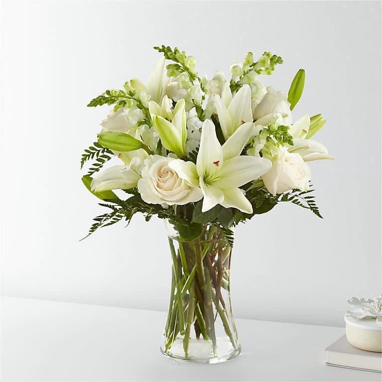 Eternal Friendship Bouquet - An exuberance of bright and beautiful white blossoms provides an exquisite way to deliver your expressions of sympathy and comfort. This life affirming tribute combines white roses, snapdragons and Asiatic lilies accented by lush greens arranged in a clear glass 8" vase. An excellent choice for a wake, funeral service or for sending your condolences to the home of grieving family or friends.  Please Note: The bouquet pictured reflects our original design for this product. While we always try to follow the color palette, we may replace stems to deliver the freshest bouquet possible, and we may sometimes need to use a different vase.