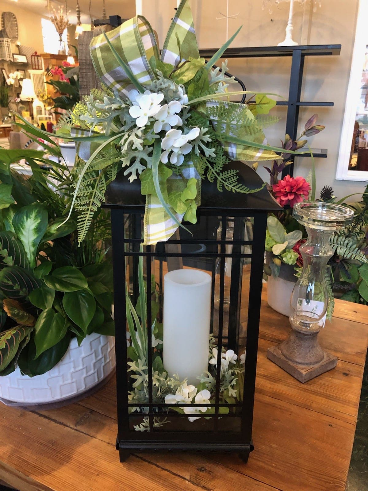 Black metal lift-top lantern - This metal black lantern is 18" tall and 7½" wide. It comes with a battery operated candle that has a timer that can be set for 4 or 8 hours. It is decorated with a pretty green and white plaid ribbon. It is accented with white silk hydrangea blossoms and assorted silk greenery.  Not for outside use.