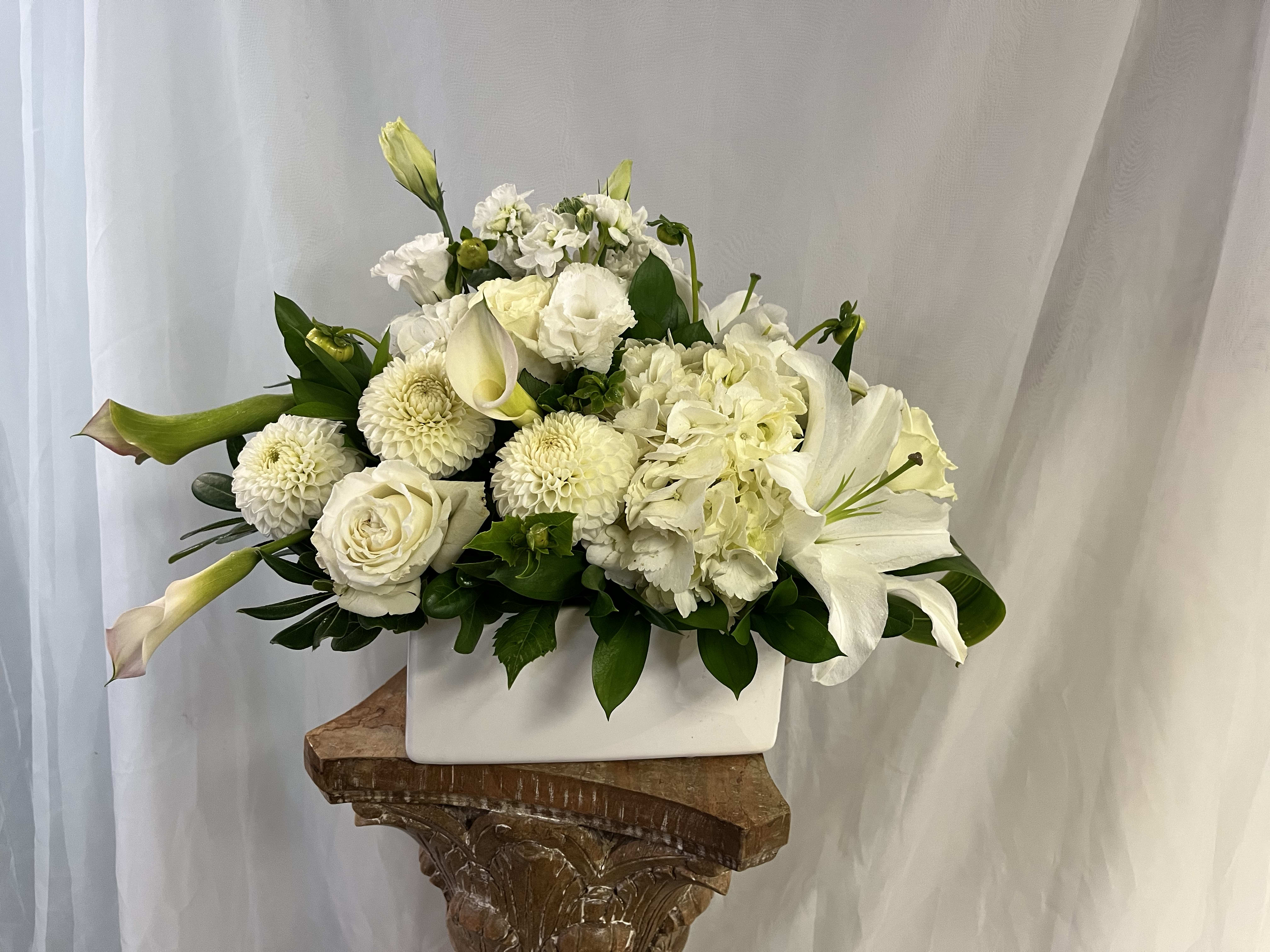 Classical White  - Lush blooms of pure white hydrangeas, roses, lilies, and delicate accents create a monochromatic masterpiece of texture and grace, symbolizing purity and peace. Elegantly presented in a modern white square ceramic vase—perfect for weddings, sympathy tributes, contemporary homes, or any occasion calling for understated luxury.