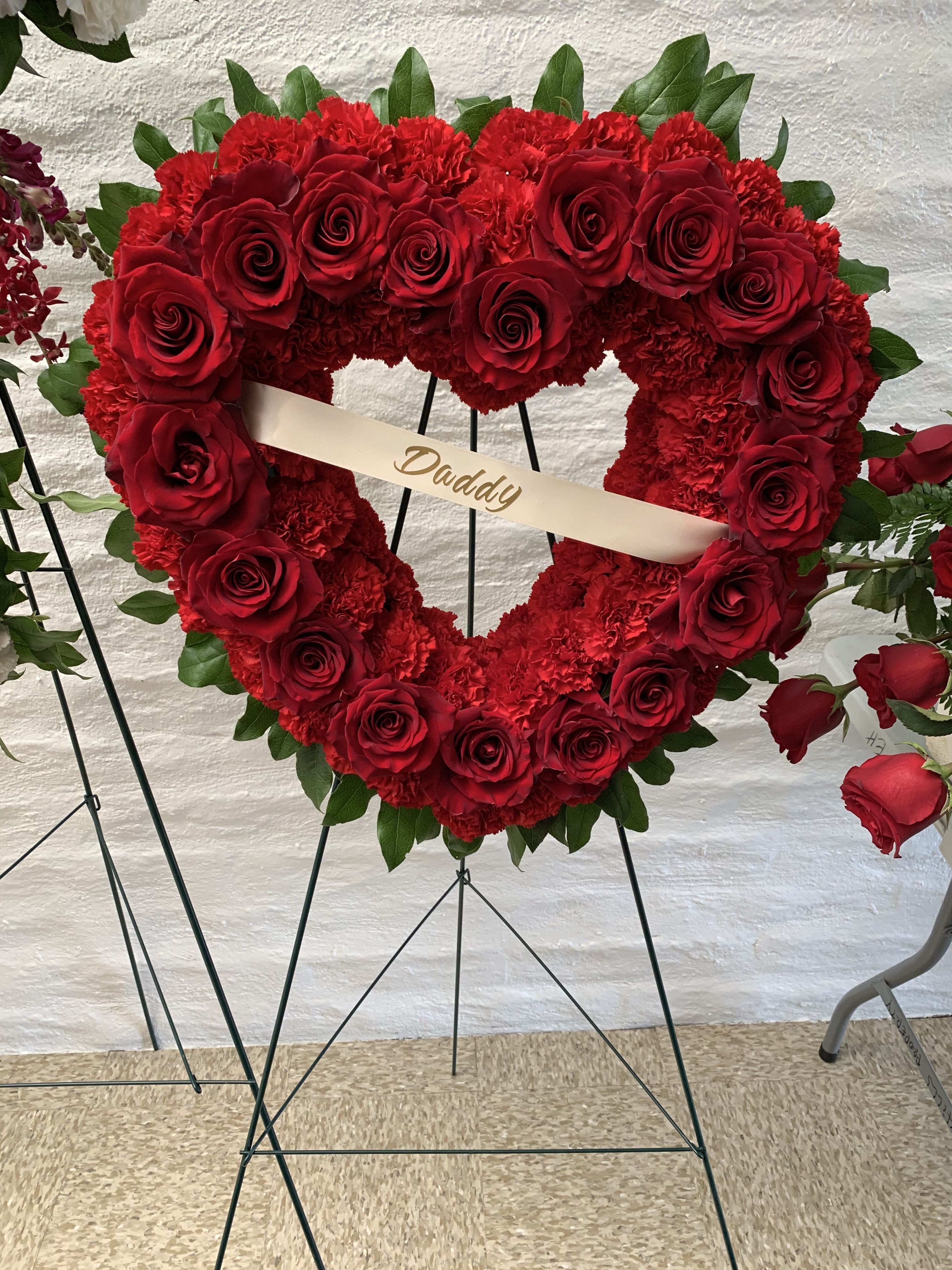 With Love - *Color modification available.   A tender expression of love and remembrance, this heart-shaped arrangement is thoughtfully designed to honor a life held deeply in the heart. Rich red roses, symbolizing enduring love and respect, are carefully placed among soft, textured blooms, forming a graceful silhouette that speaks quietly of devotion and connection.  The gentle curve of the heart reflects affection that lives on, while the lush florals offer warmth, comfort, and a sense of peace during a time of reflection. Presented with care and intention, this arrangement serves as a heartfelt tribute—one that conveys love, gratitude, and remembrance when words are not enough.