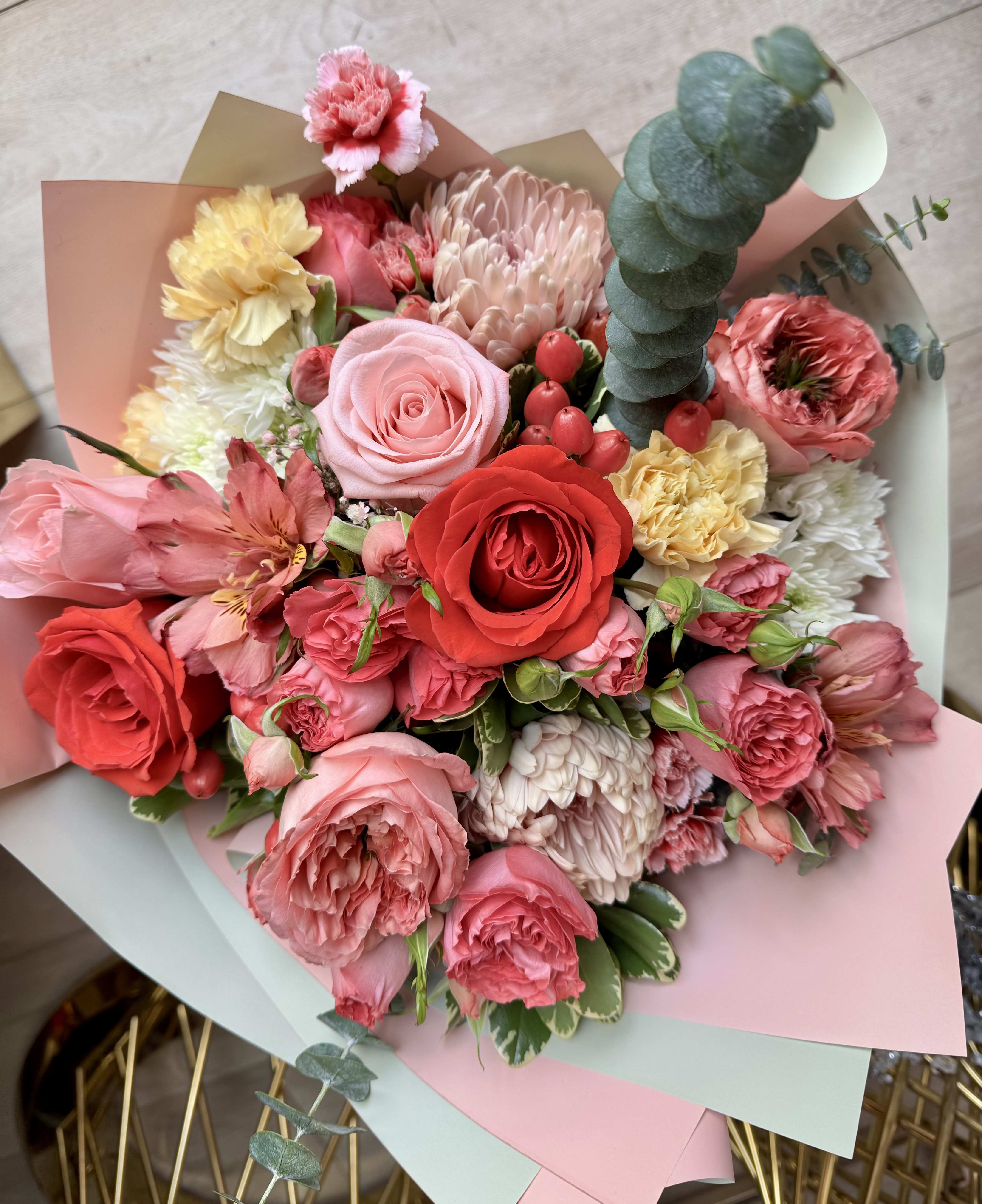 Blush &amp; Scarlet Symphony - Blush &amp; Scarlet Symphony is a romantic, garden-inspired bouquet bursting with rich textures and elegant color harmony. Featuring a stunning mix of blush and pink garden roses, classic reddish roses, soft pink spray roses, creamy chrysanthemums, delicate carnations, and seasonal accent blooms, this arrangement is beautifully balanced with fresh eucalyptus and lush greenery. Hints of golden tones and berry accents add warmth and depth, creating a bouquet that feels both luxurious and heartfelt. Wrapped in soft pastel paper, this design is perfect for birthdays, anniversaries, celebrations of love, or simply to brighten someone’s day with beauty and grace.