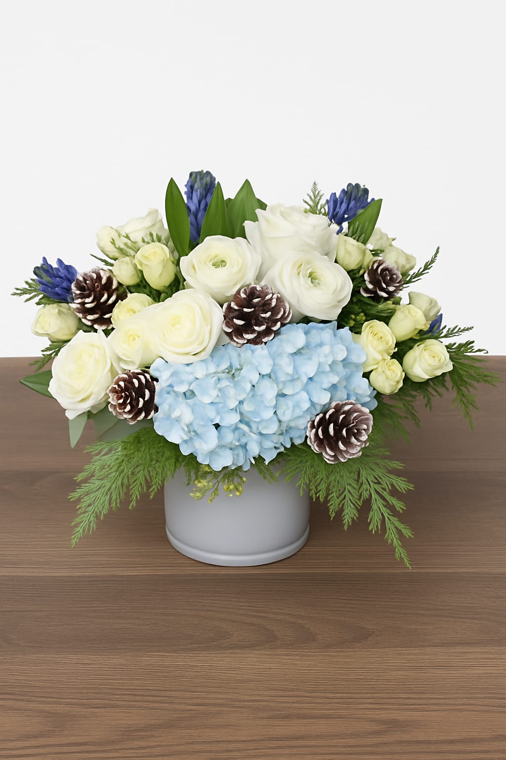 Winter Blues - A classic-styled arrangement of winter whites and blues, featuring blue hydrangea, winter white roses, ranunculus, snowy pine cones and fragrant hyacinth. 