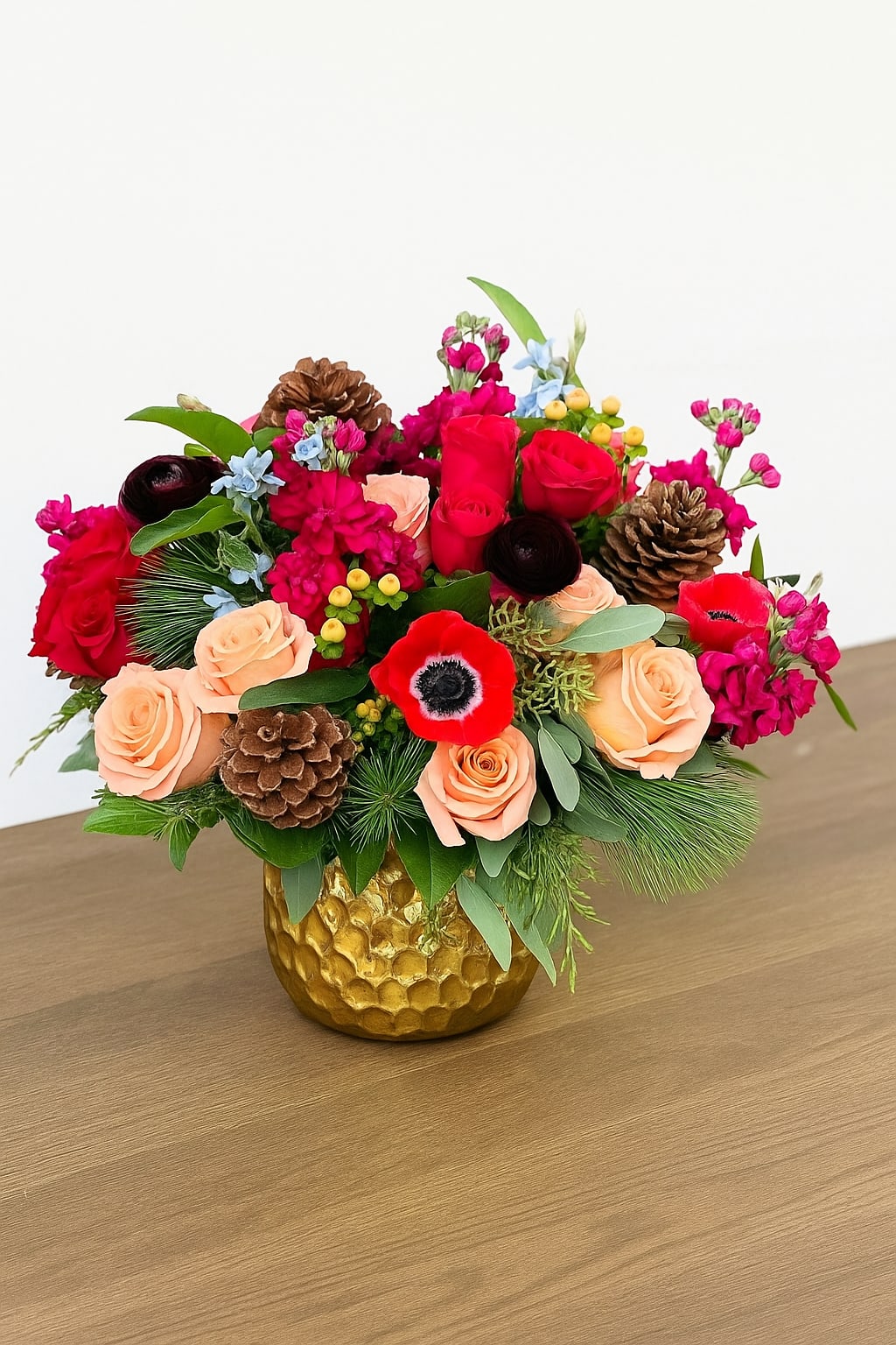 Winter Splendor - Beauty abounds in this luxurious collection of unique seasonal blooms. Arranged in a gold container, this stunning design features shimmer roses, red anenome, ranunculus and fragrant stock, artfully accented with pinecones and a unique assortment of seasonal greens.