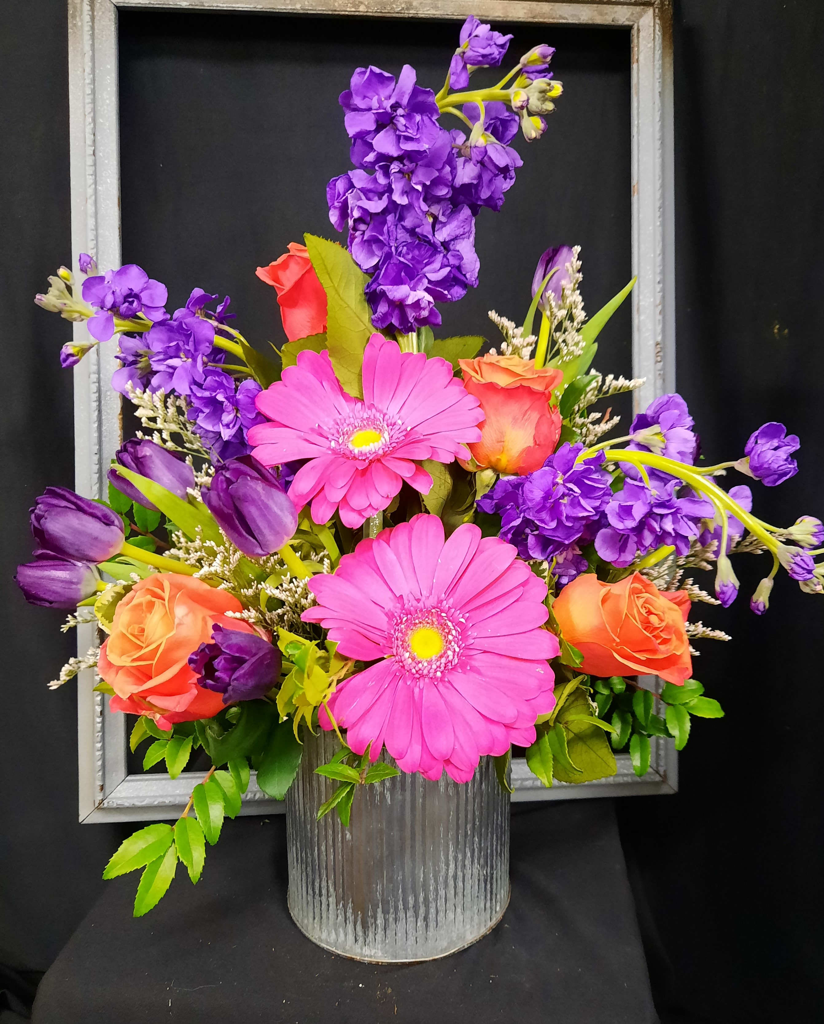 Vibrant by Gregory and Company - A corrugated container filled with bright spring flowers-gerbera daisies, stock, roses and tulips- a vibrant arrangement!