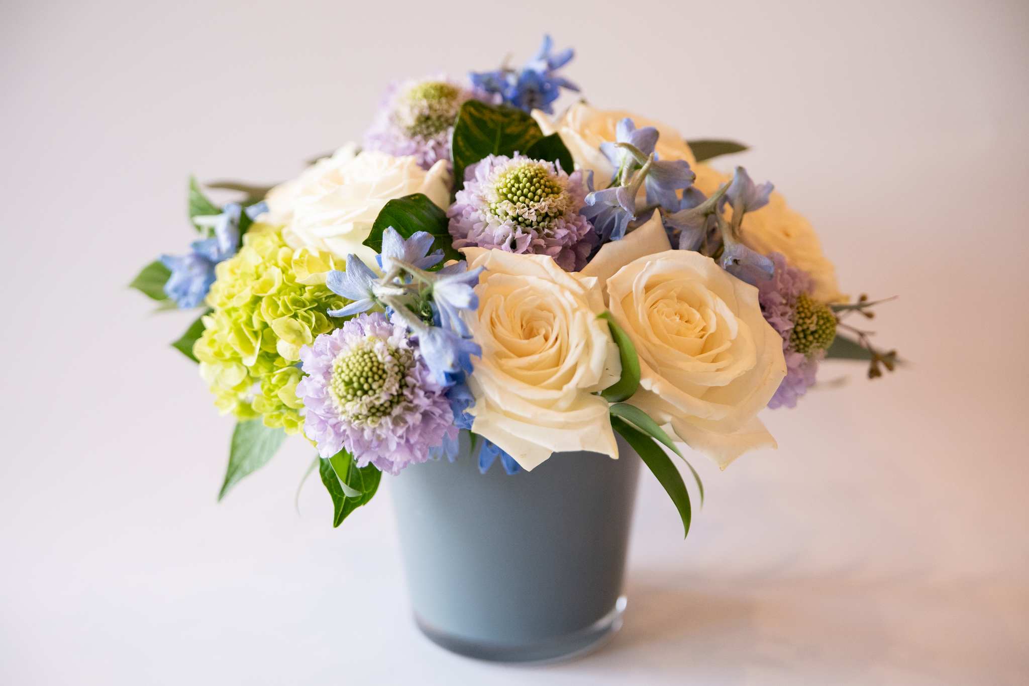 Lavender - Lavender is a floral composition made with fresh seasonal blooms that reflects the colors and feelings of the upcoming season. Delicate shades of blues, lavenders, whites and greens in glass vase.