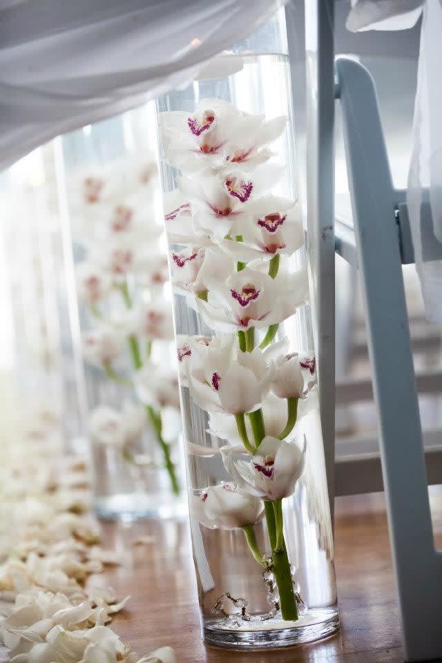 Cymbidium Symphony - a clean and modern design of cymbidium orchids set with modern white stones in a tall glass cylinder vase. This is the epitome of less-is-more and is a long lasting arrangement (approx. 2-3 weeks or more, with minimal care)