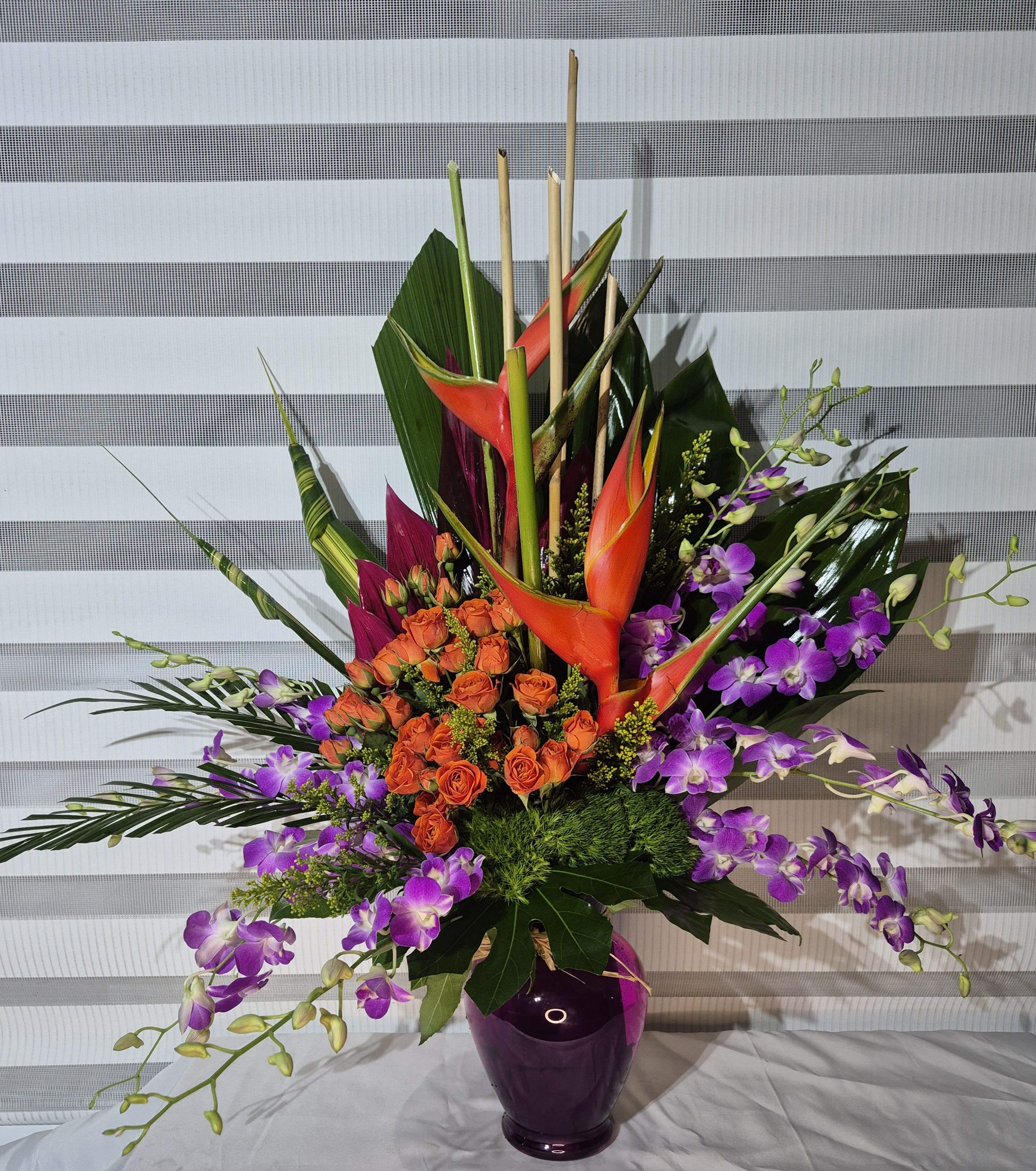 TROPICAL SPLENDOR  - A ONE-SIDED 32INS TALL TROPICAL ARRANGEMENT CONSISTING OF RED HELICONIA FLOWERS, ORANGE MINI-ROSES, LAVENDER/WHITE DENDROBIUM ORCHIDS, GREEN DIANTHUS AND EXOTIC GREENS/FOLIAGE.