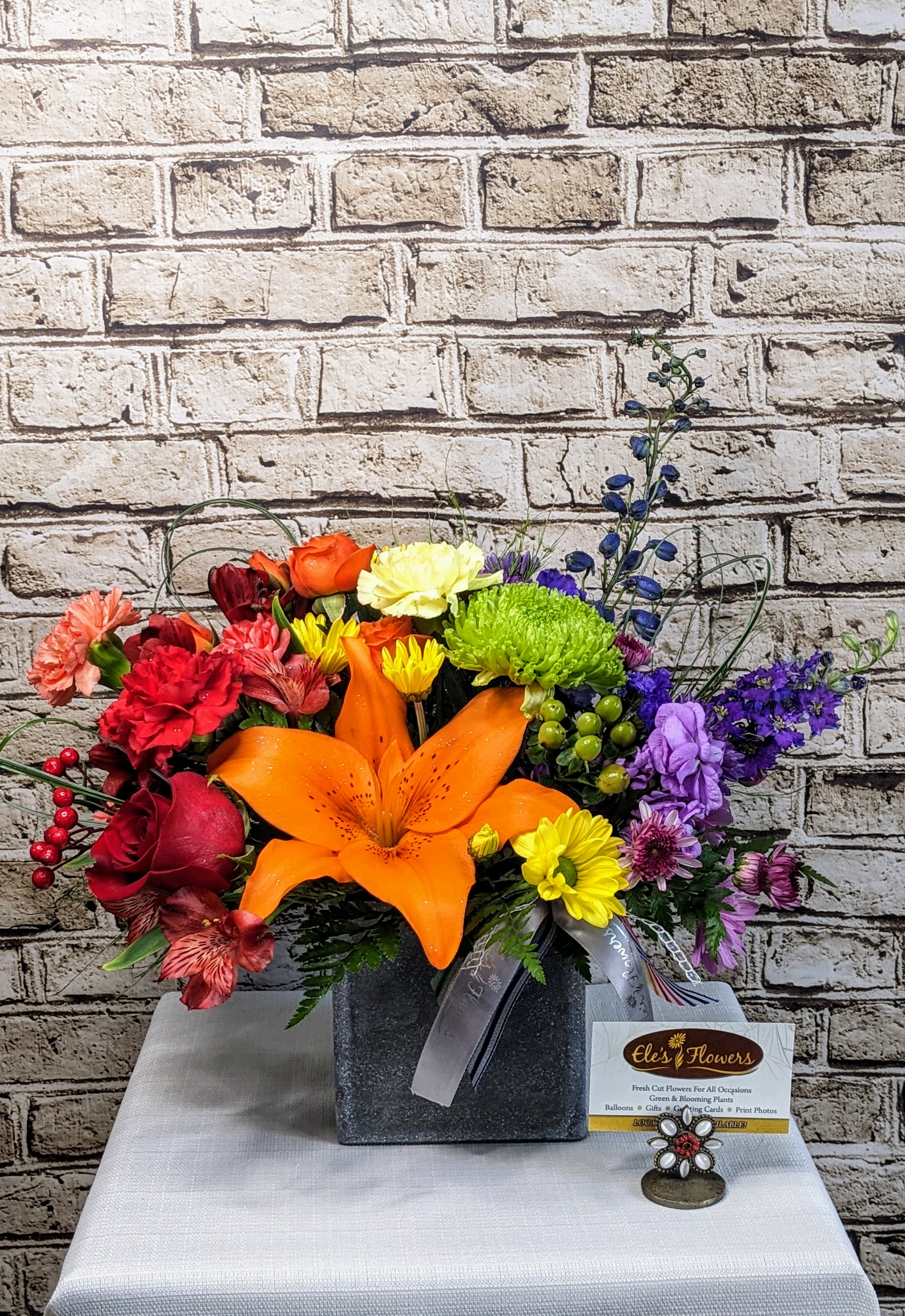 Over the Rainbow Box  - Step into a world of vibrant beauty with our Over the Rainbow Arrangement. This stunning bouquet bursts with a kaleidoscope of colors, featuring a joyful mix of fresh blooms in every shade of the rainbow. From bright reds and oranges to vivid blues, purples, and sunny yellows, each flower is meticulously arranged to create a dazzling and uplifting display. Perfect for celebrating life's special moments or adding a burst of happiness to any space, it’s a radiant expression of joy and positivity. This design comes with a keepsake box or basket and is one sided.   The designs we create are custom and the blooms and containers will vary. We use the freshest product available to create the perfect floral combination for the recipient! If you have any special requests, please add those in the "special instructions" portion of your order to help us dial in your vision. Otherwise, our skilled designers, Brett &amp; Sara, will take it from here! Please note that the photos are examples of our creations only – floral selection will vary based on what is available.  Approximate Dimensions:  Standard Size: 14"H x 10"W