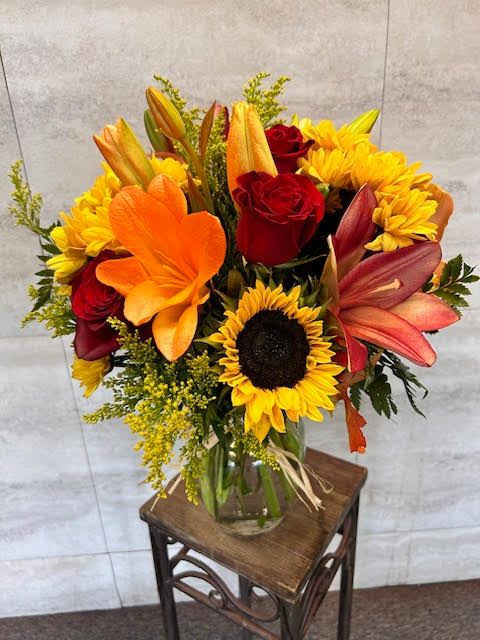 Autumn Dreams - A warm, autumn-inspired arrangement featuring sunflowers, red roses, orange lilies, and golden yellow mums, accented with seasonal filler flowers and fresh greenery. The palette is rich, bold, and vibrant, evoking a cozy fall feel.  