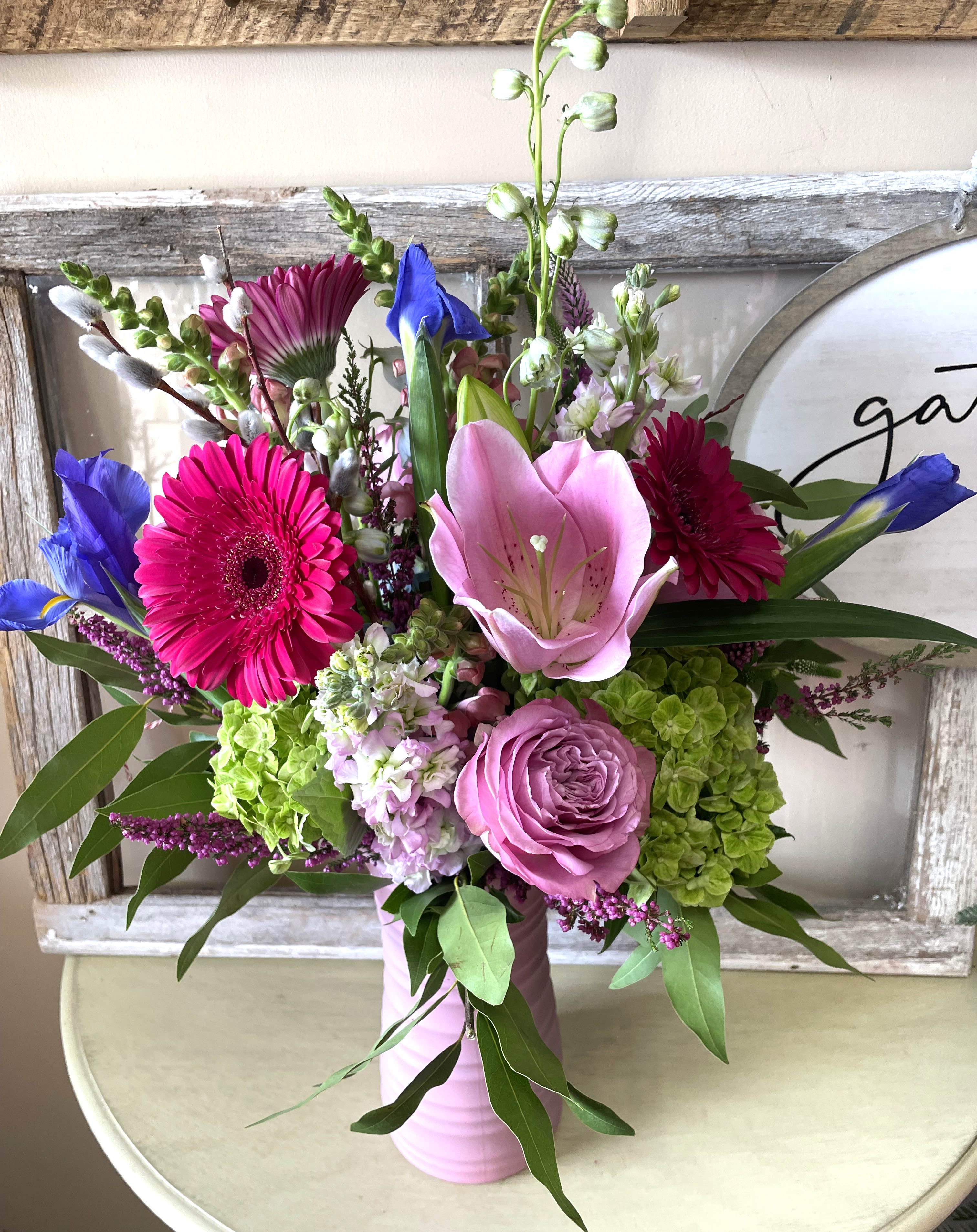 Spring Statement by The Fabulous Flower Market - A tall, vibrant arrangement featuring hydrangea, lily, iris, delphinium, snapdragons, and seasonal accents, designed with fresh greenery in a modern pink vase. Full of color, texture, and movement—perfect for making a bold spring statement.  Seasonal substitutions may apply to ensure the freshest blooms.