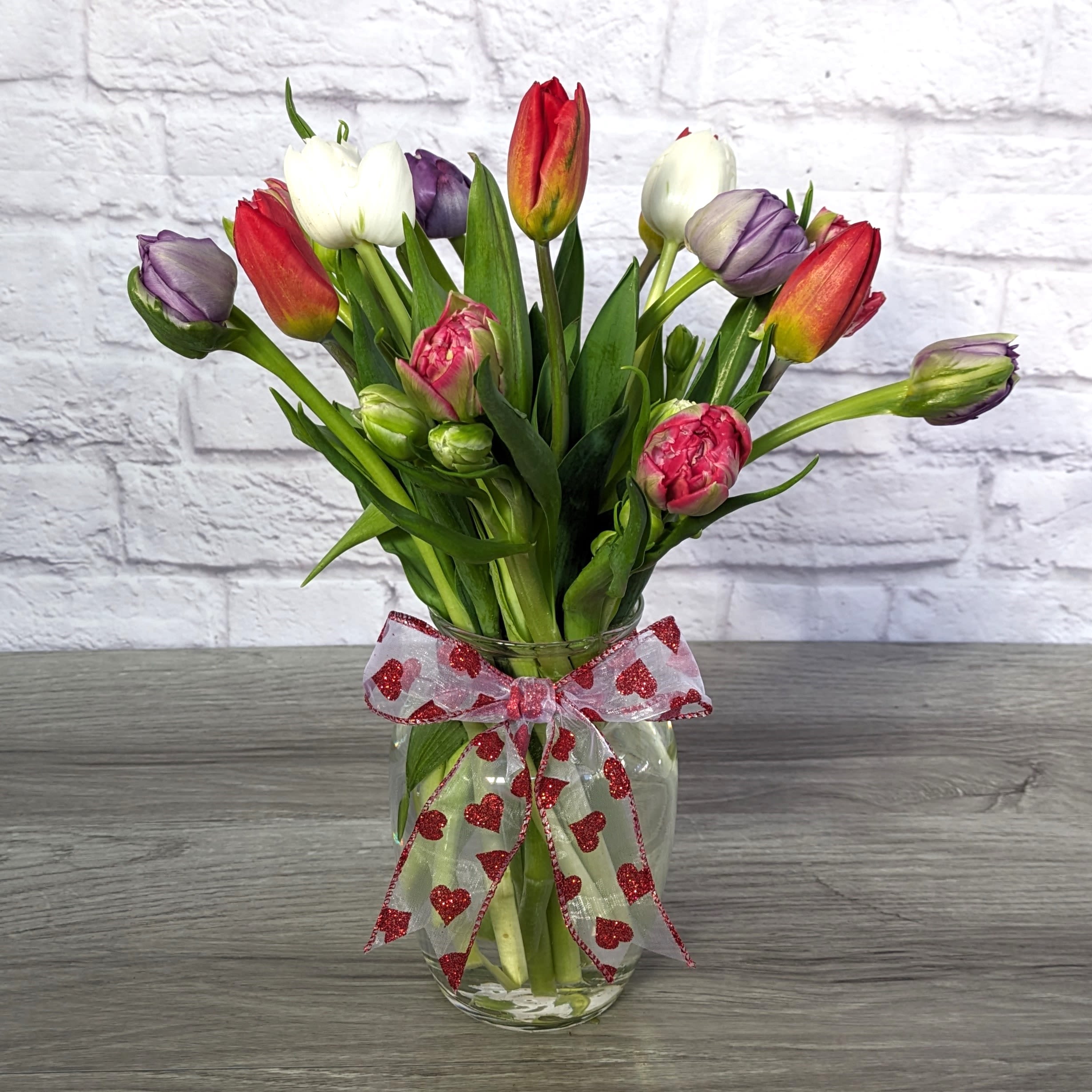 Two-Lips - Two-Lips is the perfect bouquet for the tulip lover in your life. This bouquet features a mix of tulip varieties in valentines colors,  in a 8” rose vase and tied of with seasonal ribbon.  All Round Orientation 16"H X 14"W