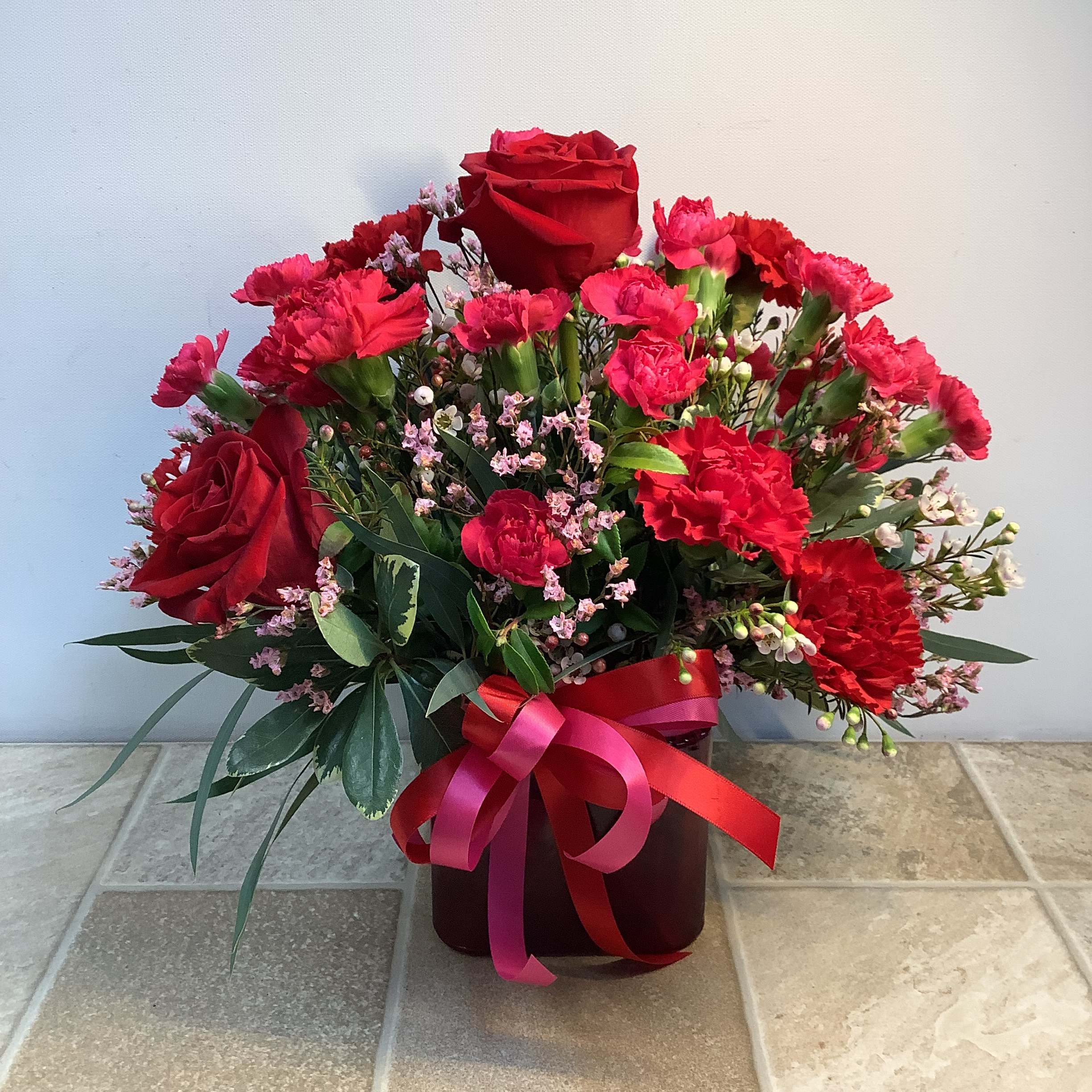 Hello Beautiful  - Surprise your someone special with this romantic arrangement of lovely red roses and hot pink and red carnations. Delicate pink limon and assorted greens add texture and fullness.  Approximate size: 14” wide x 14” tall.  Primary flowers: rose, carnation Flower delivery La Crosse, Onalaska, Holmen, West Salem, La Crescent. Flower shop. Plant store. Best florist La Crosse Wisconsin area.  Seasonal and holiday floral creations. Funeral arrangements. New baby bouquets. Birthday celebration flowers. Get well arrangements. Just because gifts.