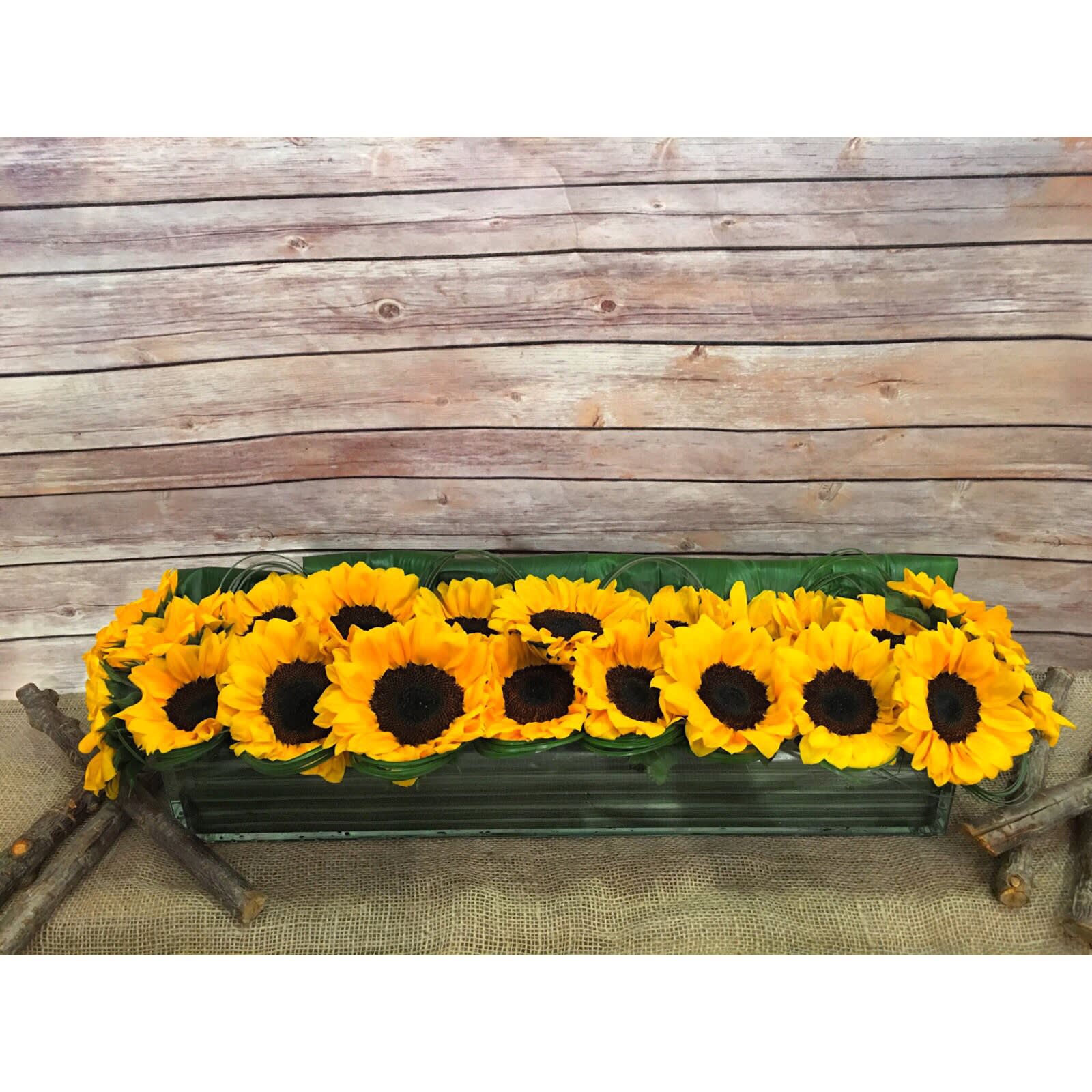 SUMMER BLISS  - STATEMENT MODERN ARRANGEMENT IN LONG RECTANGULAR GLASS VASE WITH SUNFLOWERS AND ASPIDISTRA LEAFS.