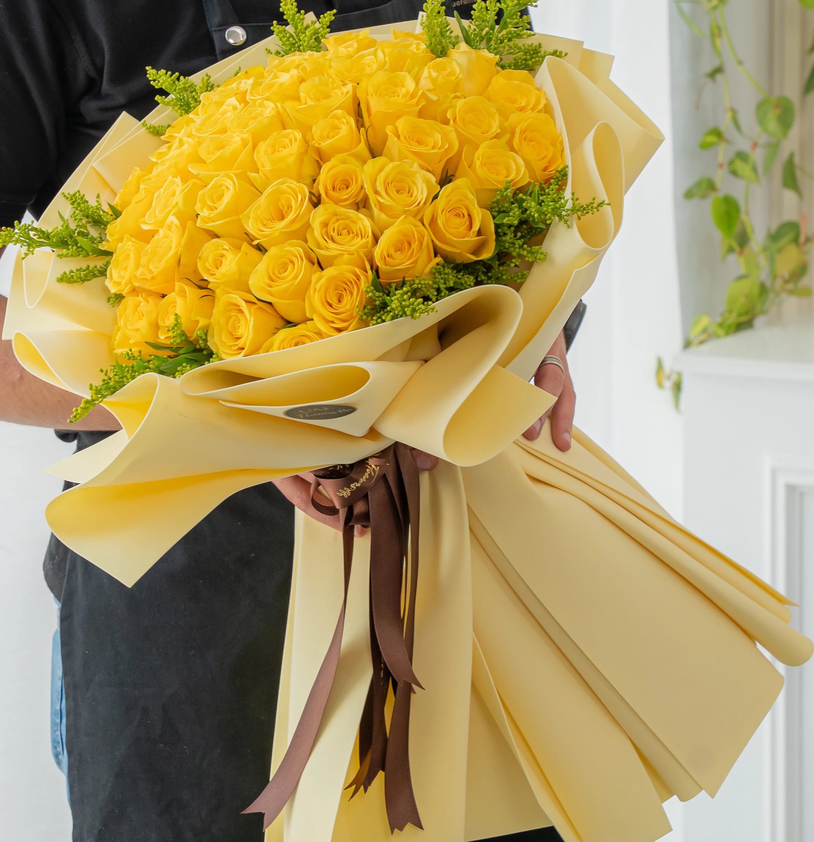 A radiant 46 Yellow Roses Wrapped bouquet  - A radiant bouquet featuring 46 elegant Yellow Roses, beautifully complemented by cheerful solidago fillers. Wrapped in vibrant yellow foam paper and tied with pretty ribbons, this bouquet brings a perfect blend of purity, brightness, and charm—ideal for uplifting someone’s day or marking a joyful occasion.