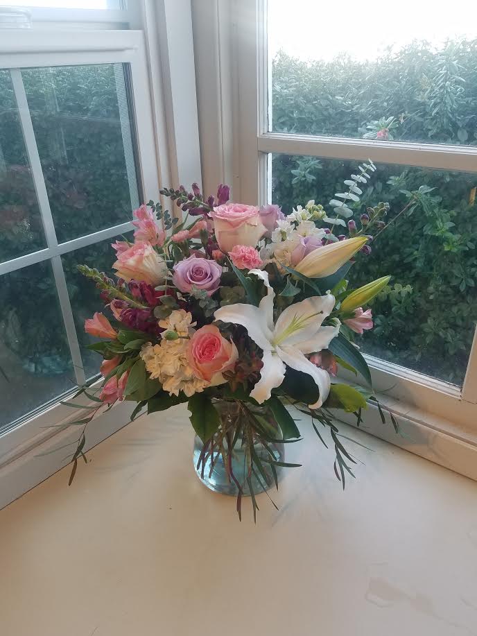 Unchained Melody - A soft and romantic design.  Fragrant white oriental lilies, lavender and pink roses, white stock, and touches of burgundy snapdragons add some depth to the color palette.  Baby blue eucalyptus and burgundy agonis eucalyptus add fragrance and structure.  As always, we may have to substitute flowers, greens, or the container based on what we have in stock.