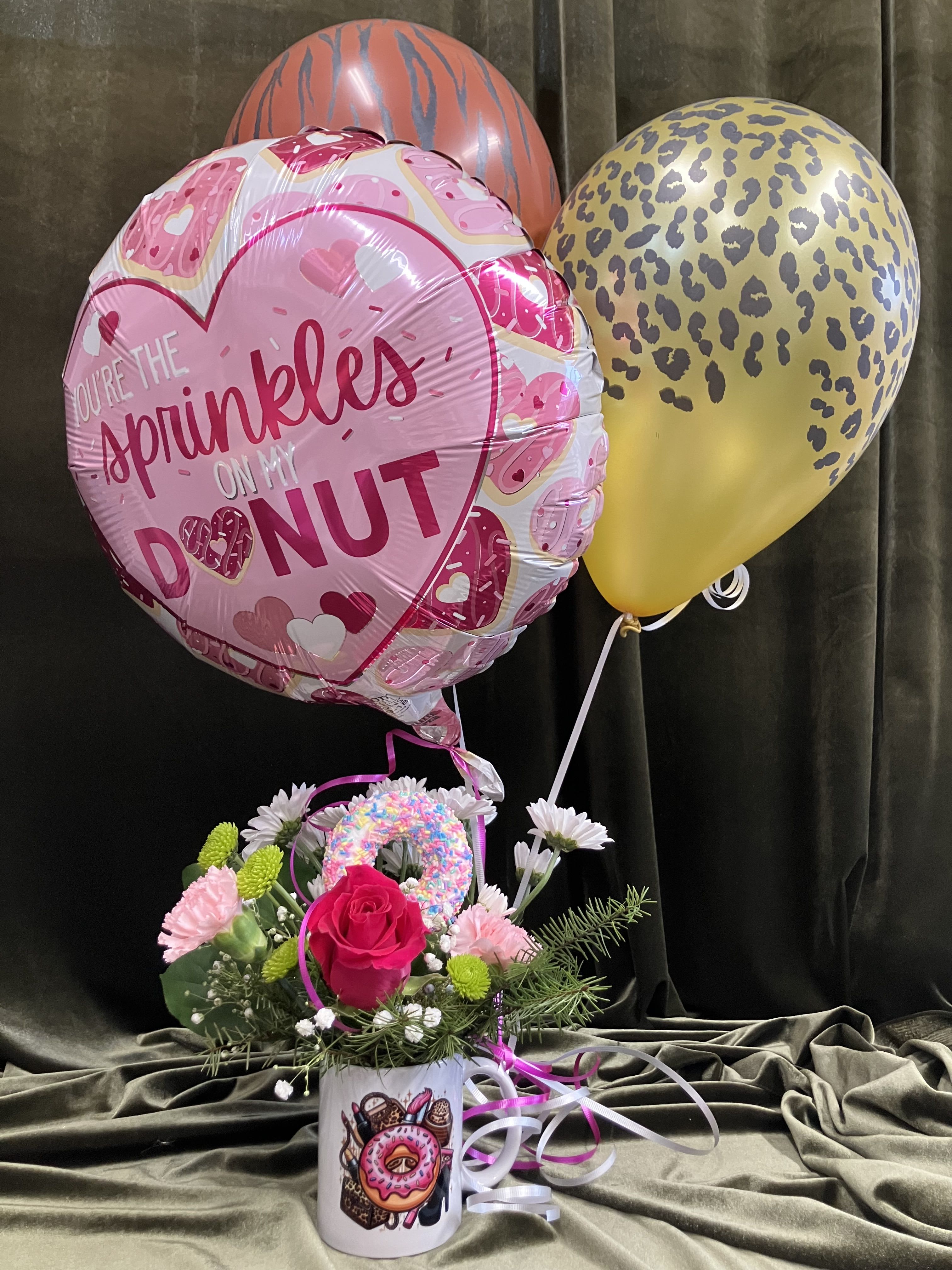 Be My Sprinkles  - Cute donut mug with hot pink rose, pink carnations, green poms, daisies and baby’s breath and a faux donut.  Paired with a Mylar balloon and two animal print latex balloons makes this a super fun valentine gift!