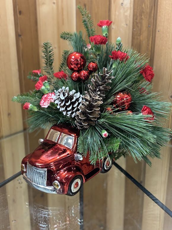 Holiday Ride of Cheer" - This charming little red truck is filled with a festive arrangement of Christmas cheer! Perfectly nestled in the bed of the truck are vibrant red poinsettias, fragrant evergreens, and sprigs of holly, accented with sparkling ornaments and a touch of snow. This delightful holiday centerpiece brings a nostalgic touch of vintage charm to your home, making it the perfect gift or decor for the season. Whether placed on a mantle or as a table centerpiece, it’s sure to bring warmth and joy to any holiday setting!  Ideal for adding a dash of whimsy and a whole lot of holiday spirit to your Christmas celebration. 