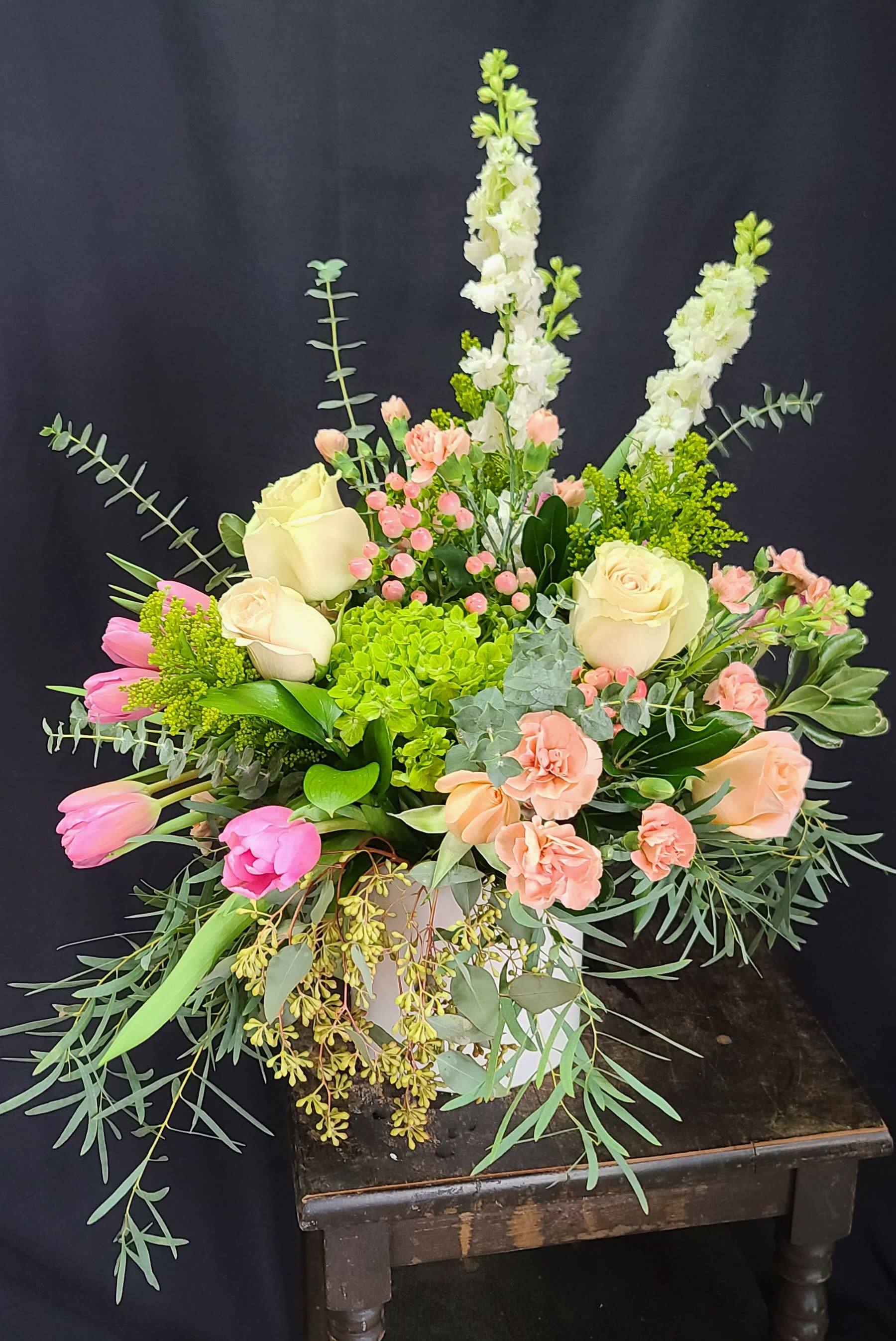 Eternal Glory  - Stunning, lush eco-friendly arrangement of green Hydrangea, creamy roses, pink hypericum, pink tulips, pink mini carnations,  white larkspur, golden aster and a sea of lush eucalyptus' of baby blue, willow, seeded, and feather. The reusable ceramic container is overflowing with lush blooms and we don't use any floral foam with this type of container making it earth friendly. 
