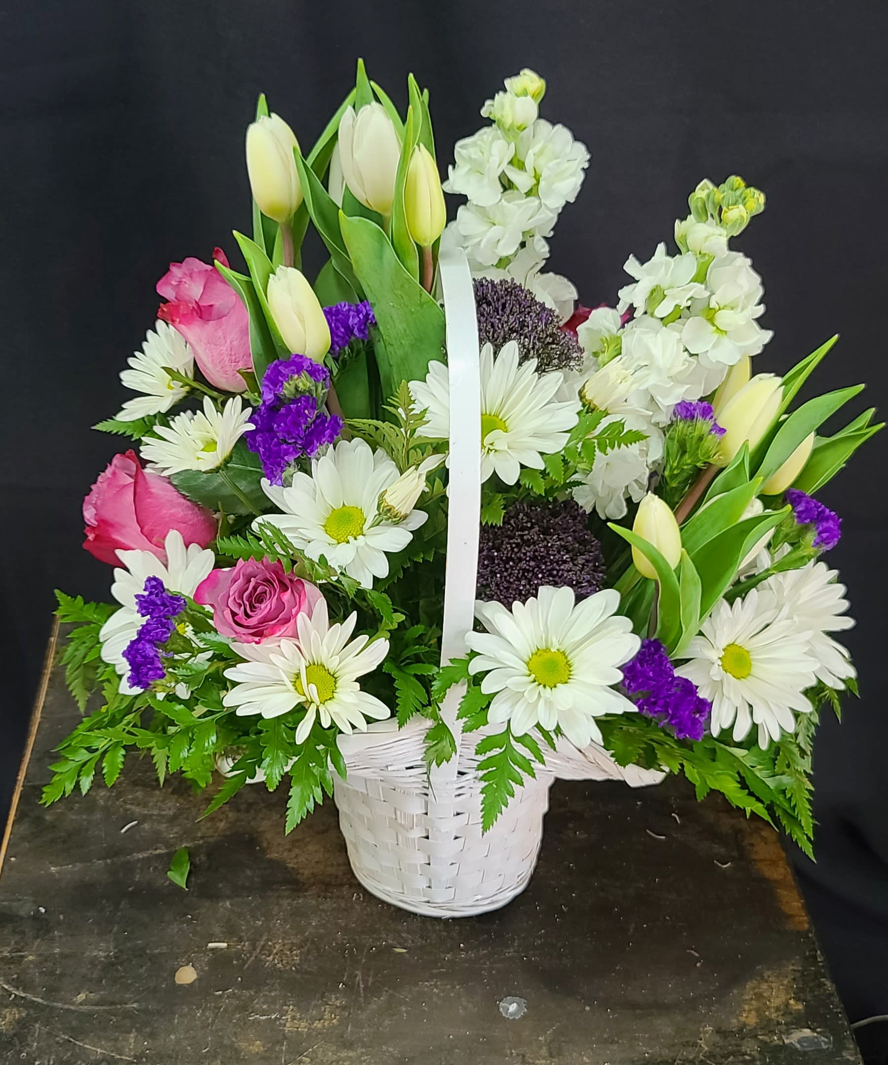 Spring Basket - A fresh spring basket filled with tulips, stock, roses, and daisies. Colors may vary by availability. 