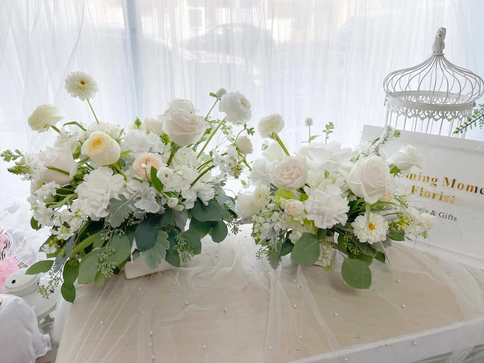 [Fresh Flower] Pure White Serenity - Seasonal white flowers with greens in cube vase  The approximate dimensions are as follows: Basic size measures 8"W x 8"H x 8"D Deluxe size measures 15"W x 11"H x 10"D.