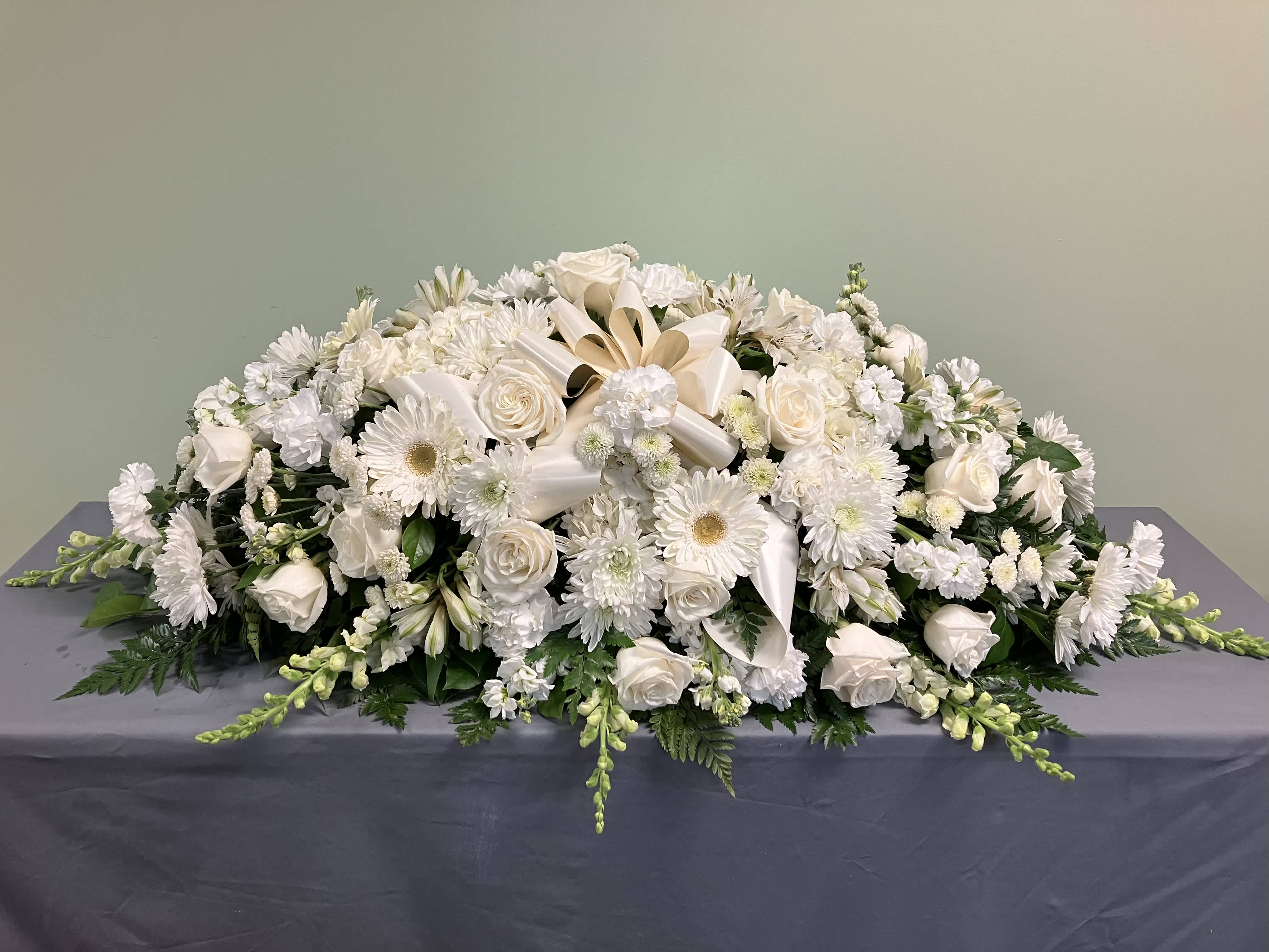 White Casket Spray C1 - Serene, Devoted, Loyal. Those are some of the adjectives that this spray evokes. Ivory roses are cushioned in white hydrangea, gerber daisies and white stock.