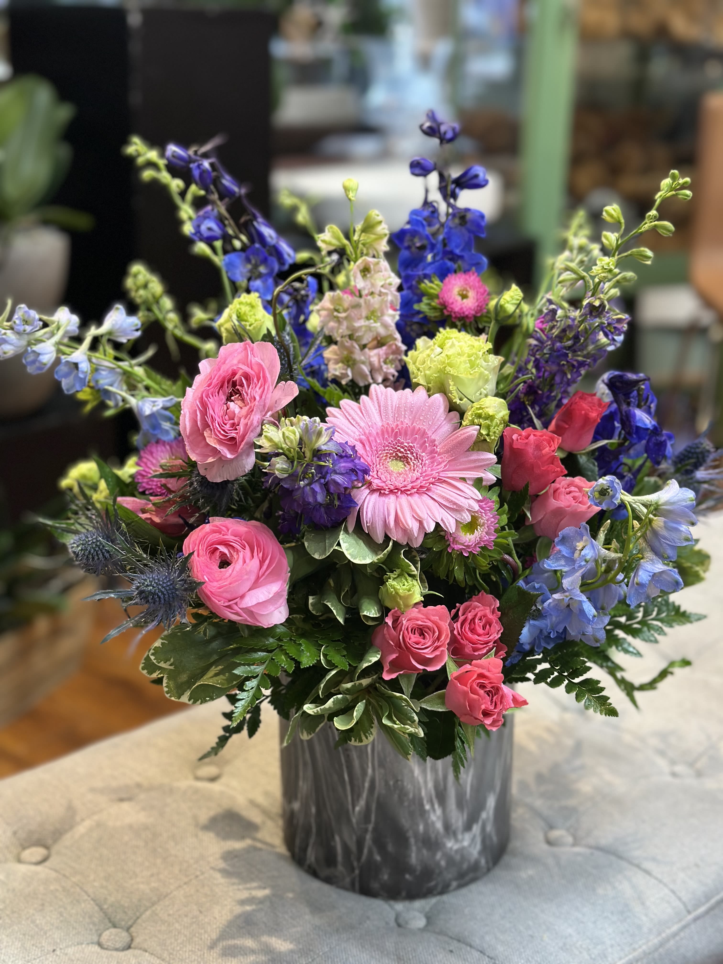 Midnight Garden - Midnight Garden is a striking floral arrangement where bold meets beautiful. With rich indigo delphinium, soft pink gerbera daises, ranunculus, and vibrant green accents, this design captures the enchanting mystery of a twilight bloom. Artfully arranged in a modern charcoal marbled vase, it's perfect for making a statement-elegant, lush, and full of personality. Ideal for celebrations, thoughtful gestures, or simply to elevate any space with effortless charm.