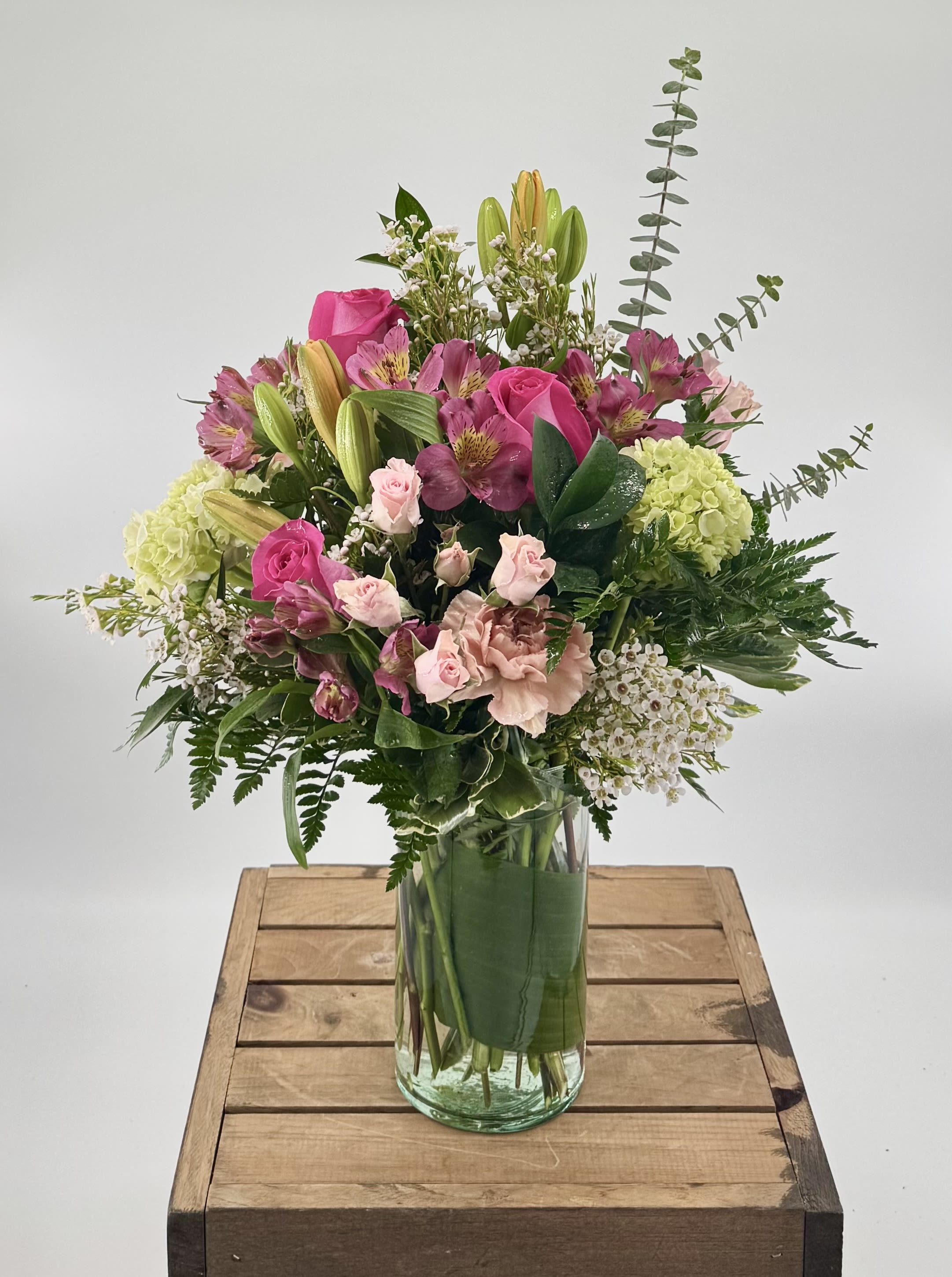 Blush Life (BB) - Introducing "Blush Life," a delightful flower arrangement that combines vibrant shades of orange and pink to create a harmonious and stunning display. This arrangement features a captivating blend of orange lilies, pink roses, mini pink spray roses, pink alstroemeria, mini green hydrangea, lush greenery, and filler flowers, all artistically arranged in a traditional style vase.