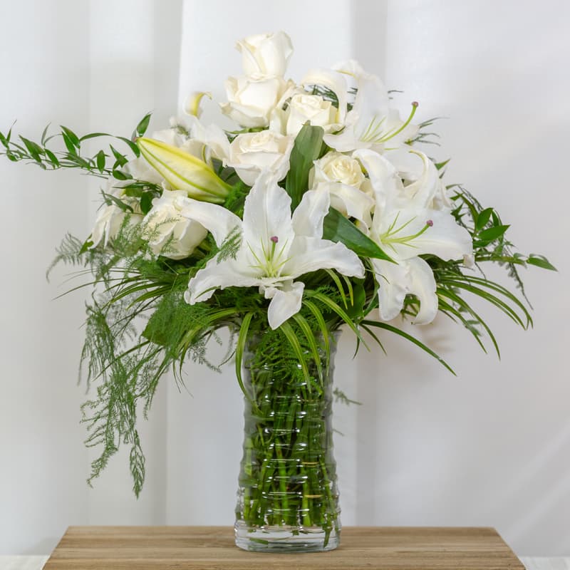 Enchanted Love - White Casablanca lilies complimented by 12 stunning white roses and seasonal greens arranged in a tall glass vase. This will WOW the recipient for any occasion.