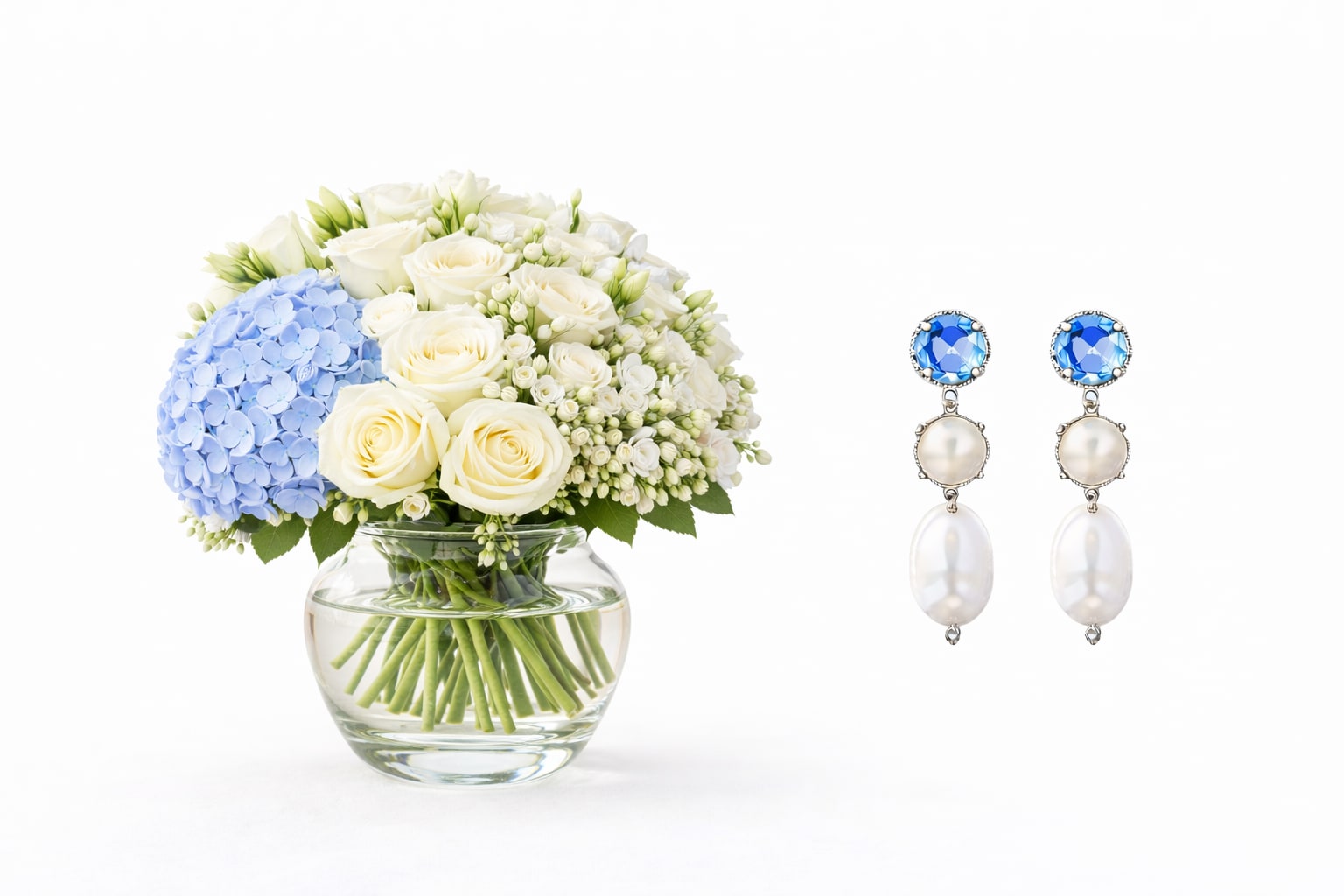 Valentine by the Beach Package - A fresh coastal - inspired Valentine's gift that blends soft florals with subtle sparkle. Includes blue hydrangea and white roses in a clear glass vase and  Sorrelli fine jewelry earrings, Standard pricing Hand designed with a light beach inspired palette Perfect for a romantic Valentine's gesture with timeless style and charm. Deluxe pricing- arrangement, lisianthus added with Sorrelli Necklace Premium pricing-arrangement with Sorrelli Necklace and Earrings 