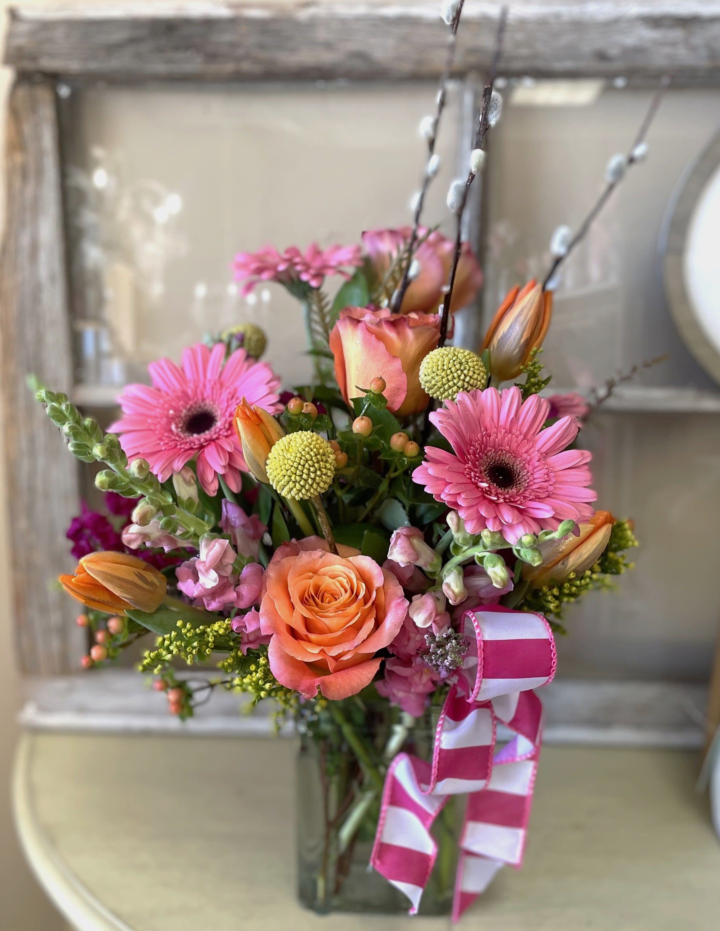 Springs First Smile by The Fabulous Flower Market - Soft pinks, peach tones, and fresh seasonal blooms come together in this bright and uplifting arrangement. Designed with gerbera daisies, roses, tulips, and textural greenery, it’s a perfect expression of late winter giving way to early spring.
