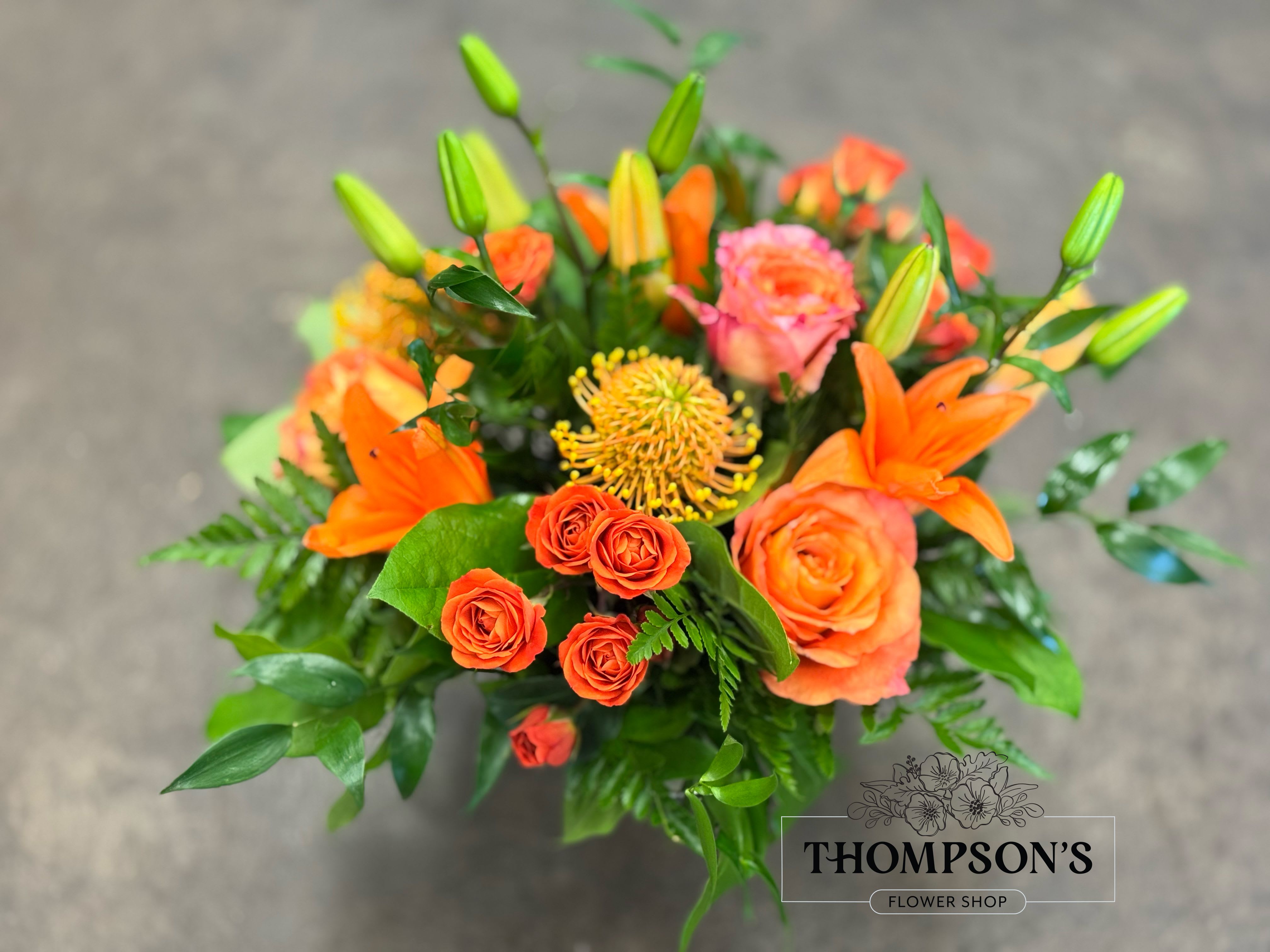 Alani - A monochromatic mix of oranges that includes pin-cushion protea, free spirit roses, spray roses and lilies. 