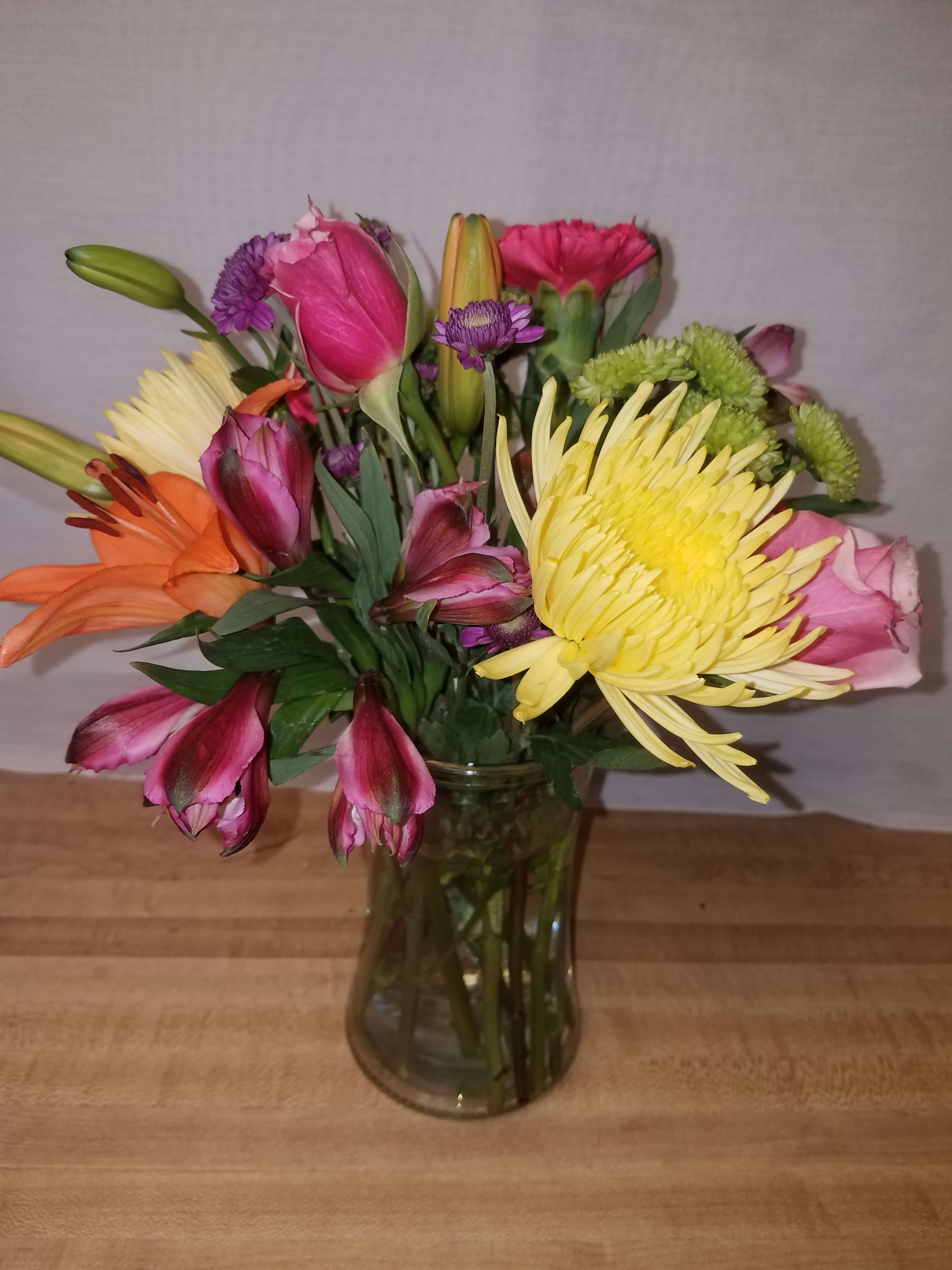 Colorful Embrace - A 6" gathering vase that sends a hug and warn wishes.  Compact enough to fit in any space they have with the colors that would make anyone smile. Approximately 12" high and includes, roses, lily, mums, button poms, and alstroemeria in assorted colors.