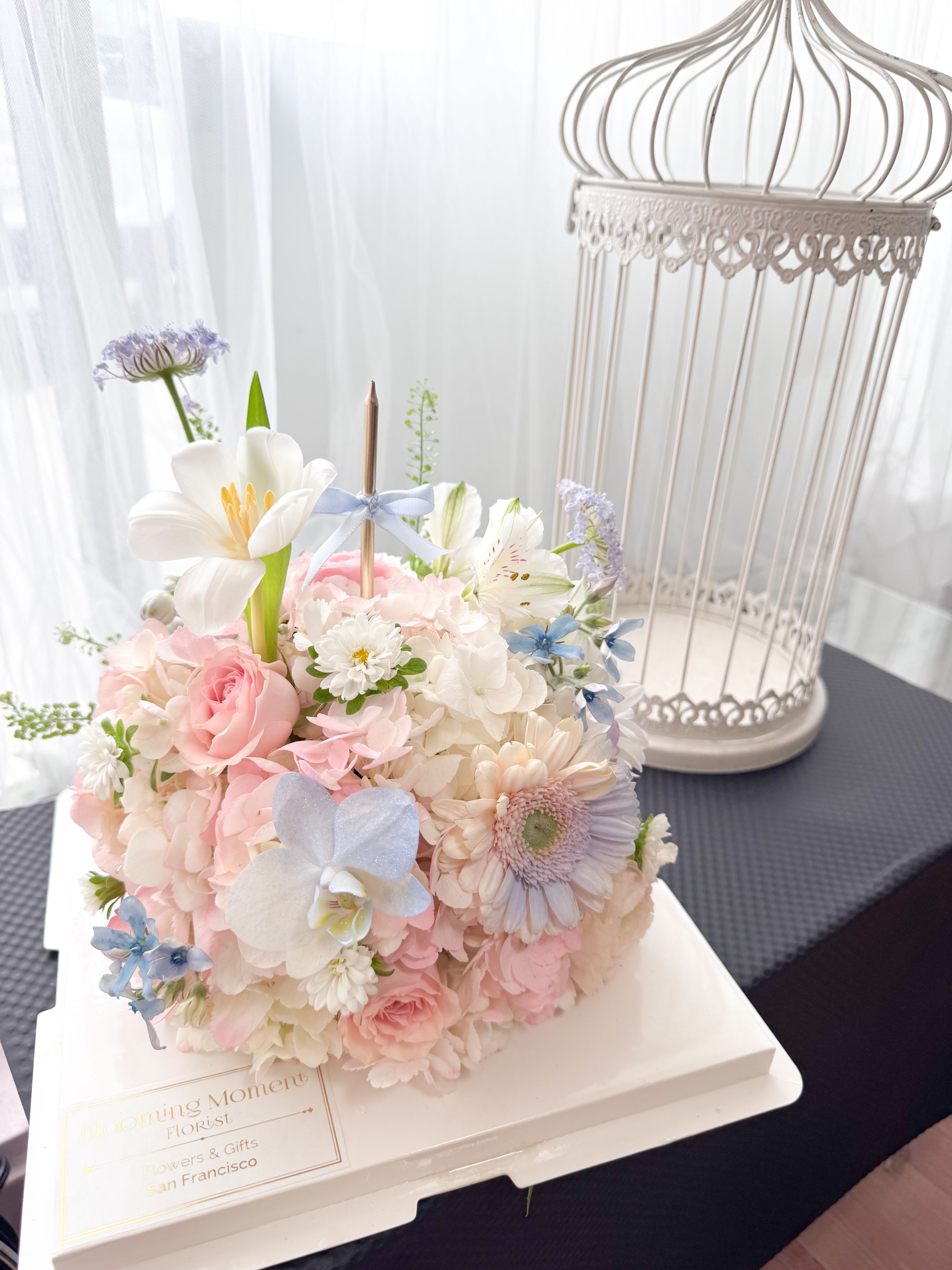 [FRESH FLOWER] Cotton Candy Theme Birthday Cake Shape arrangement - Please note: This is a flower arrangement, not edible. Celebrate life’s sweetest moments with this dreamy pastel “cake” made entirely of flowers. Featuring soft shades of pink, baby blue, and white, this arrangement is lovingly crafted to resemble a real cake — but it’s all beautiful blooms! Topped with a candle for that perfect birthday touch, it’s a charming and unforgettable way to say happy birthday or you’re special.  Whimsical, delicate, and full of joy, this floral cake makes a stunning centerpiece or gift that brings smiles without the calories.  Box: 10" x10" x10" With clear PVC outer cake box. Flower: 8"x8"  1 Candle is included. 